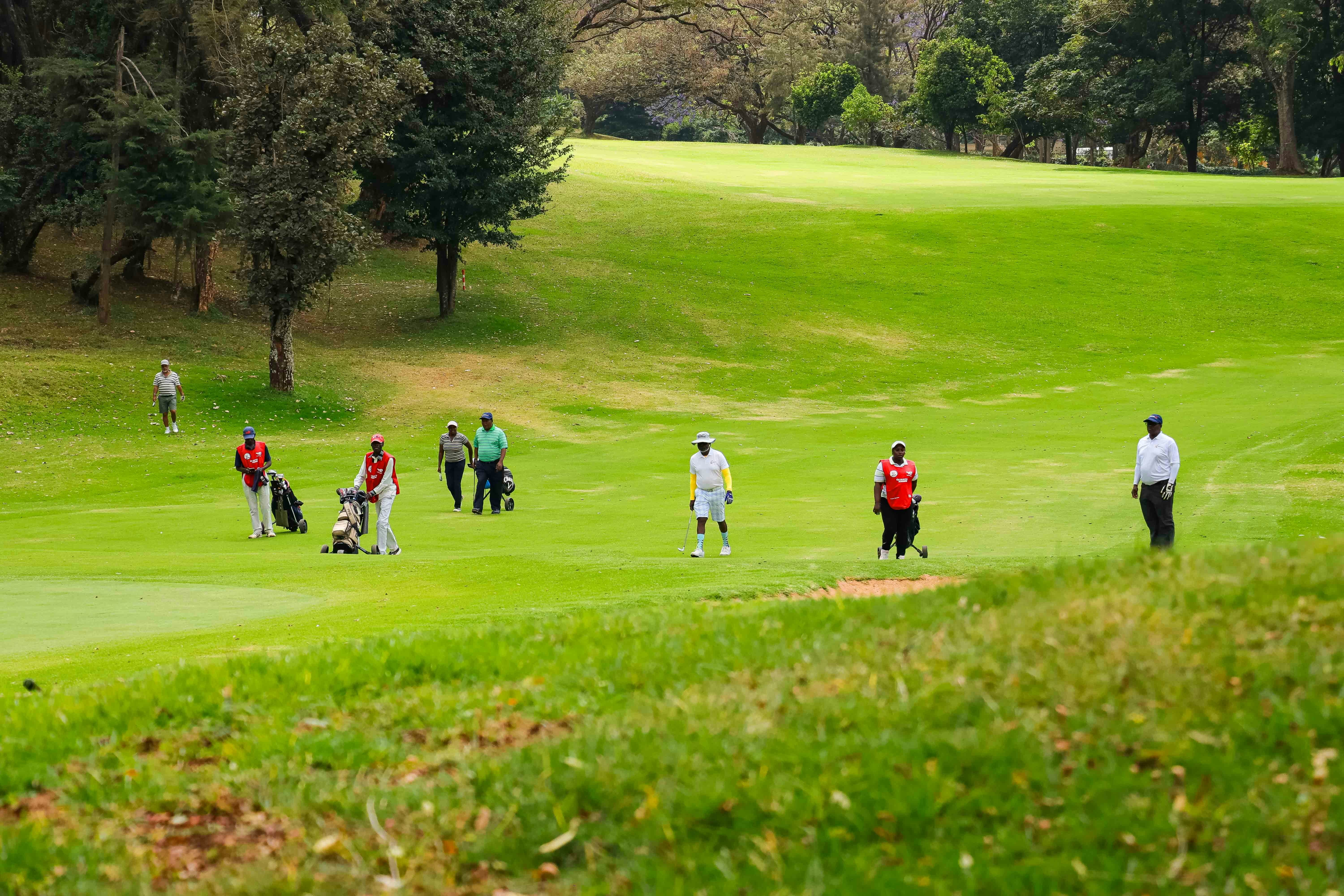A group of golfers and caddies walking across a green golf course fairway