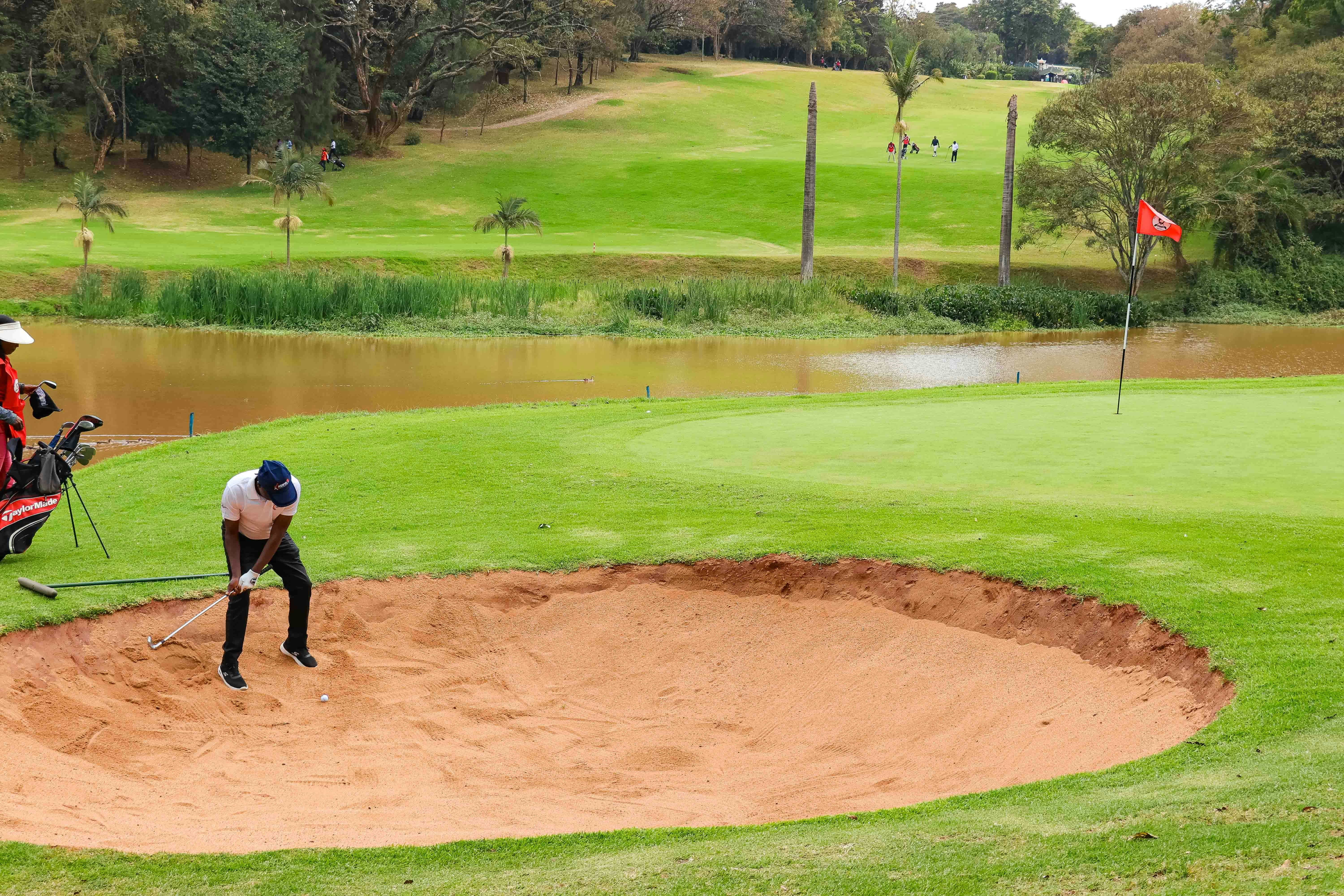 A golfer hitting a ball from a sand bunker on a green golf course
