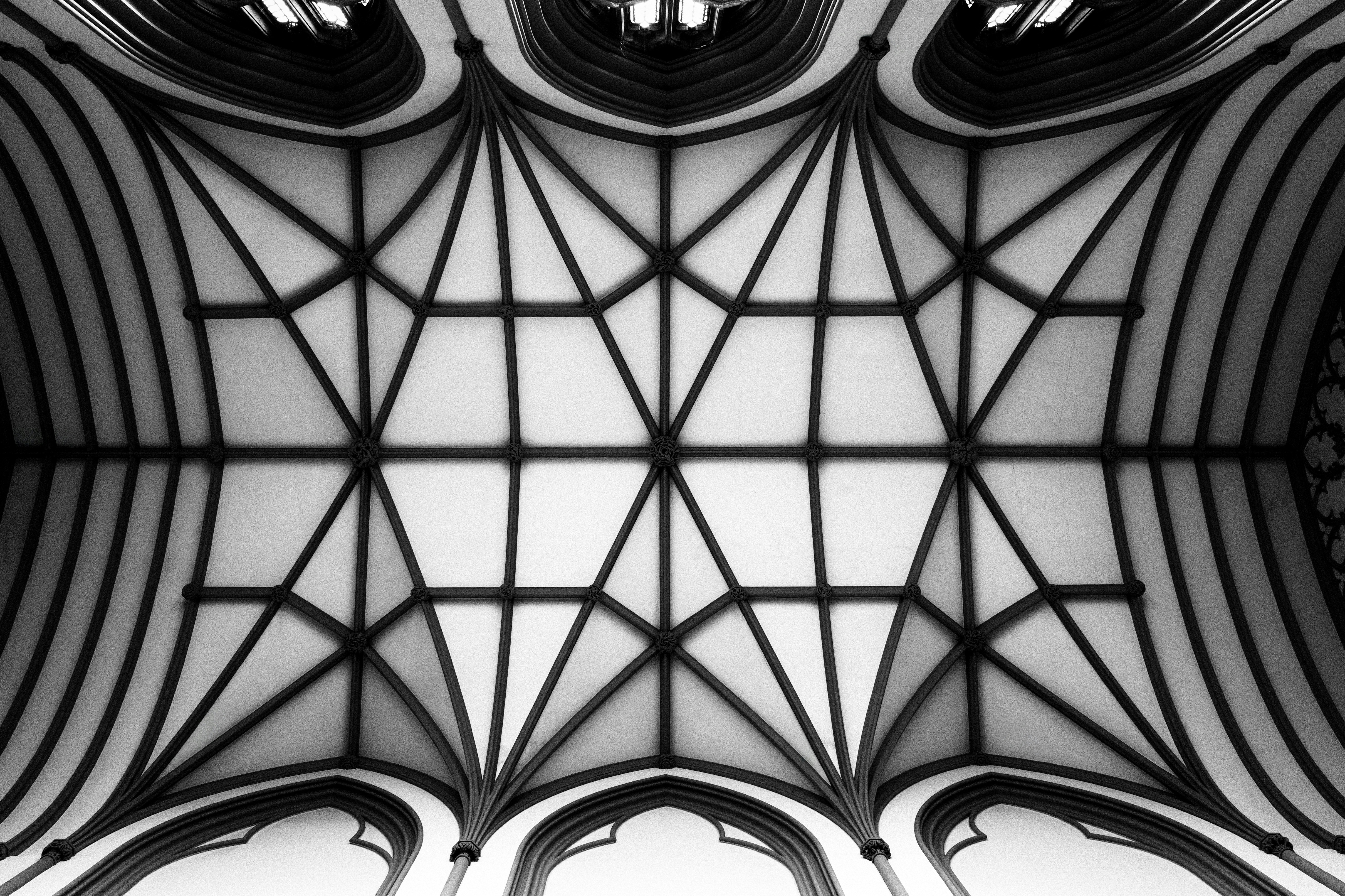 Monochrome architectural ceiling featuring a tessellated lattice of arches and ribbed vaults, photographed to emphasize symmetry and line work.