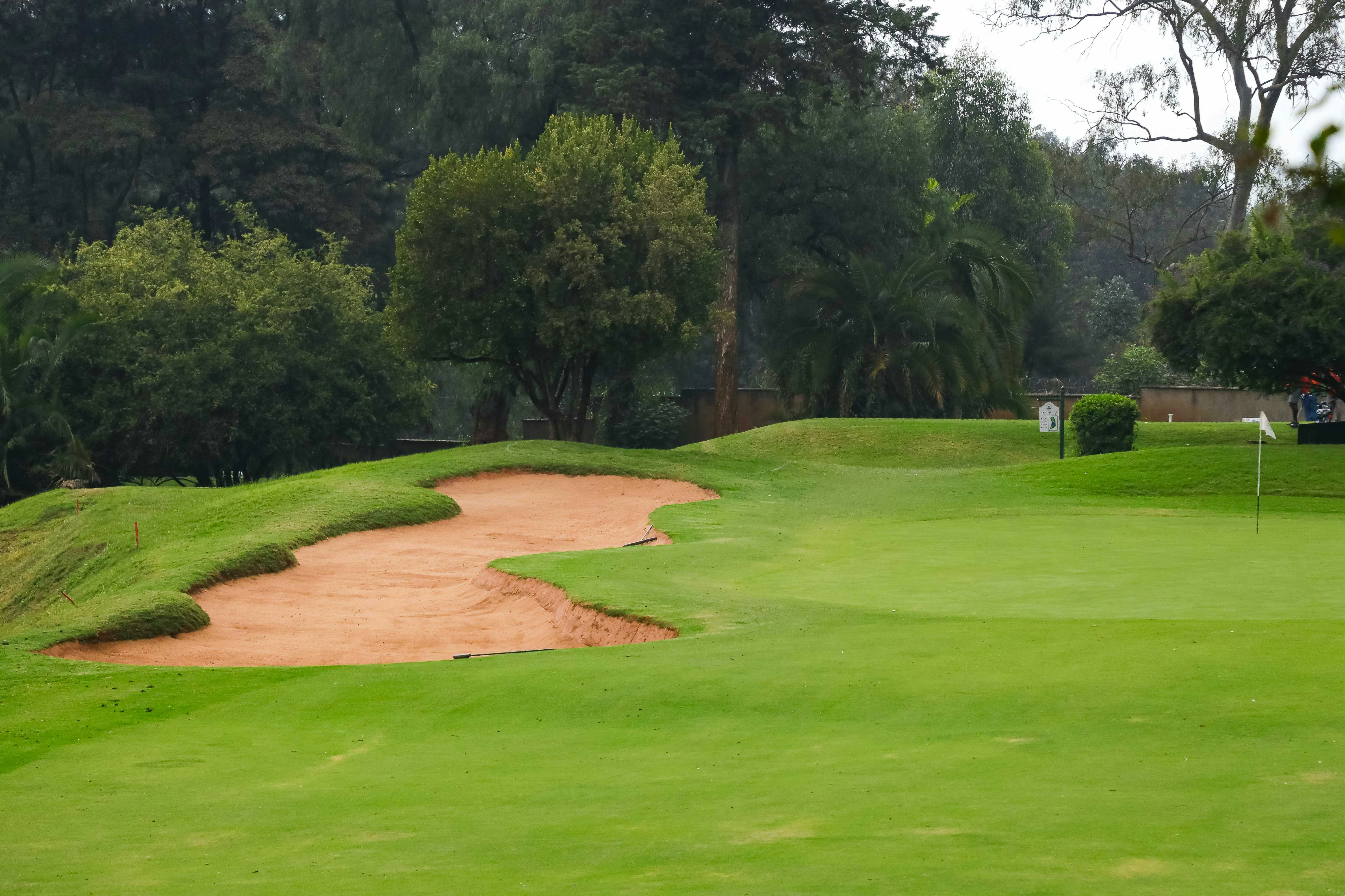 A sand bunker on a green golf course with trees in the background