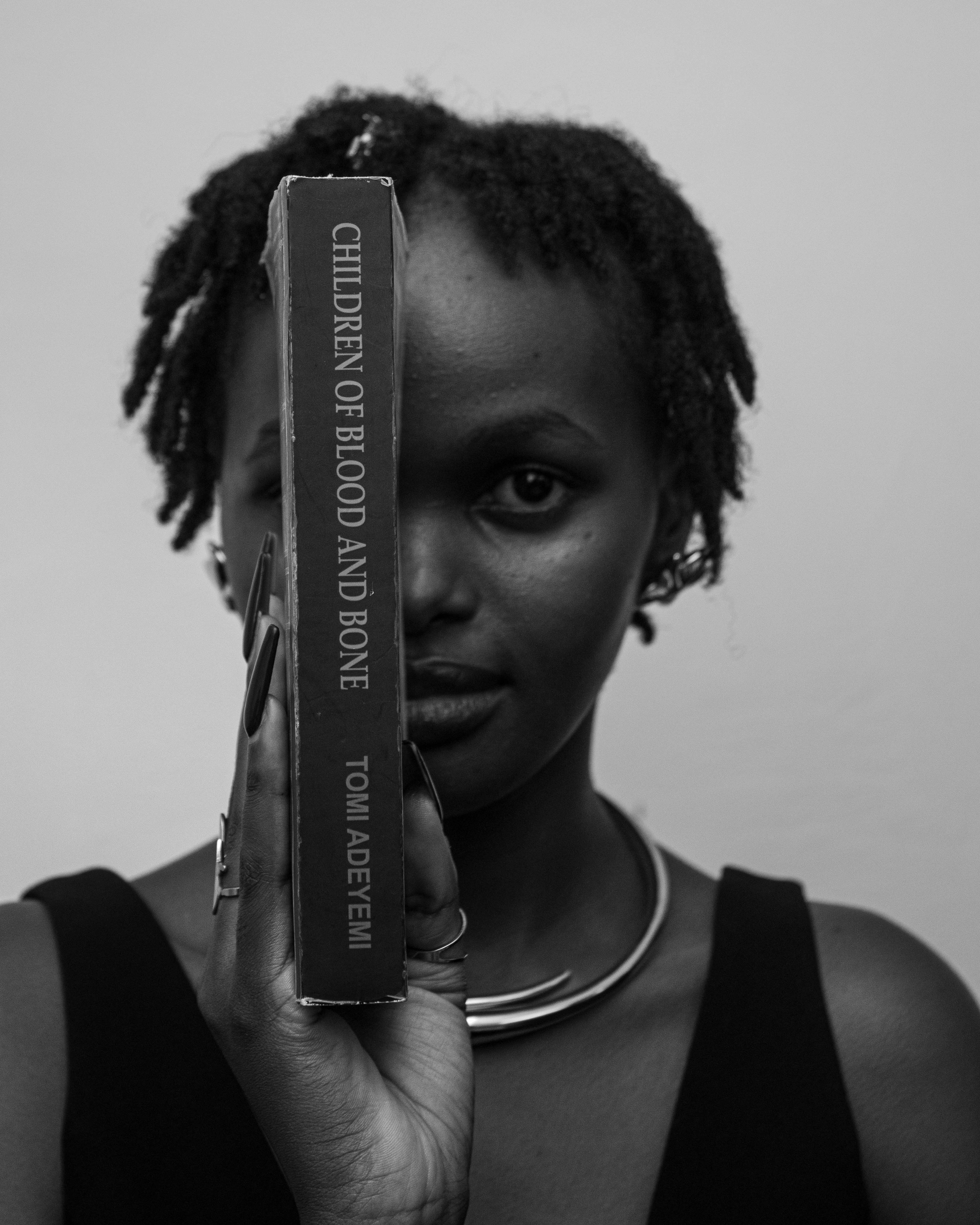 A person holding a book vertically in front of their face in black and white
