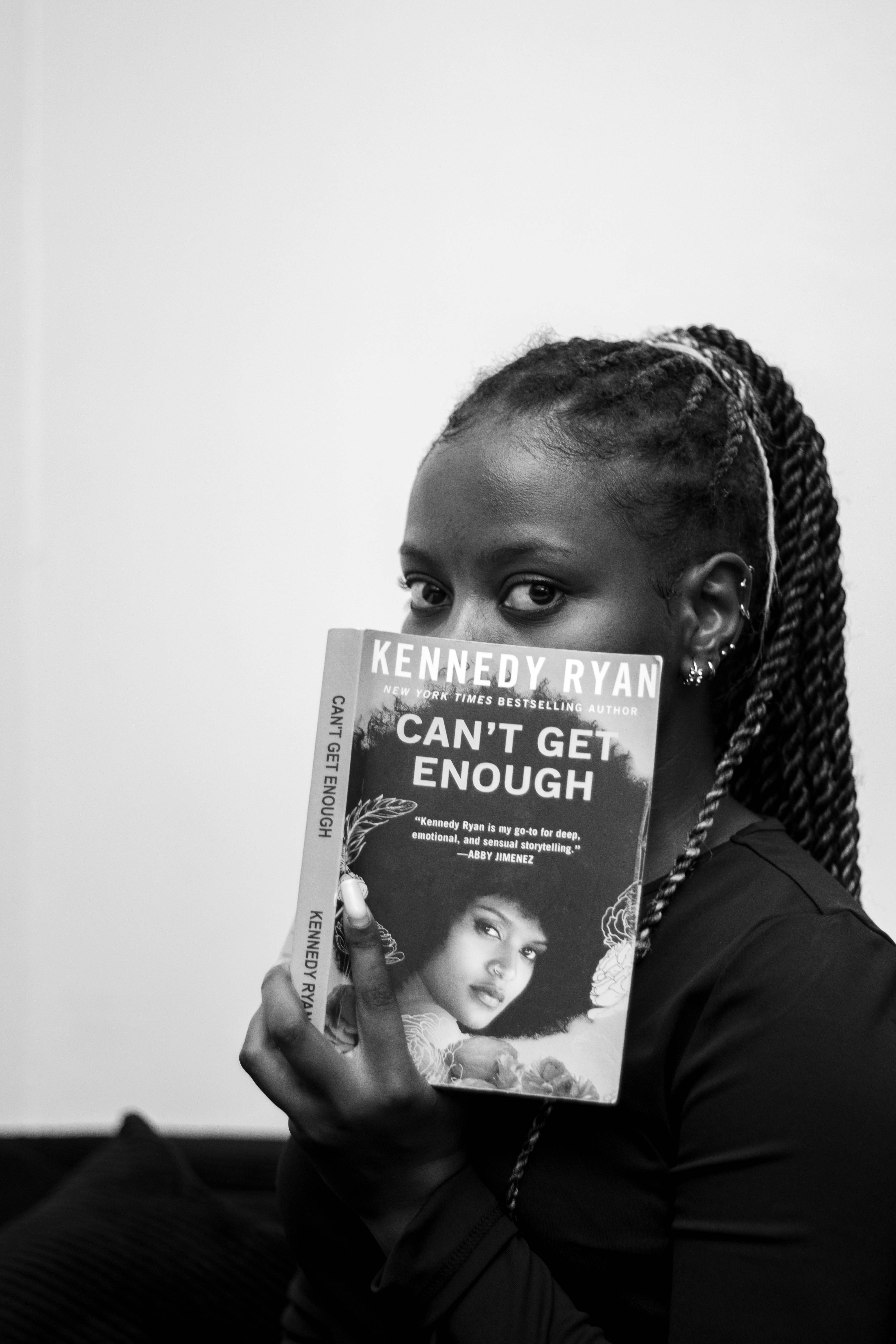 A person holding a book titled Can't Get Enough in front of their face