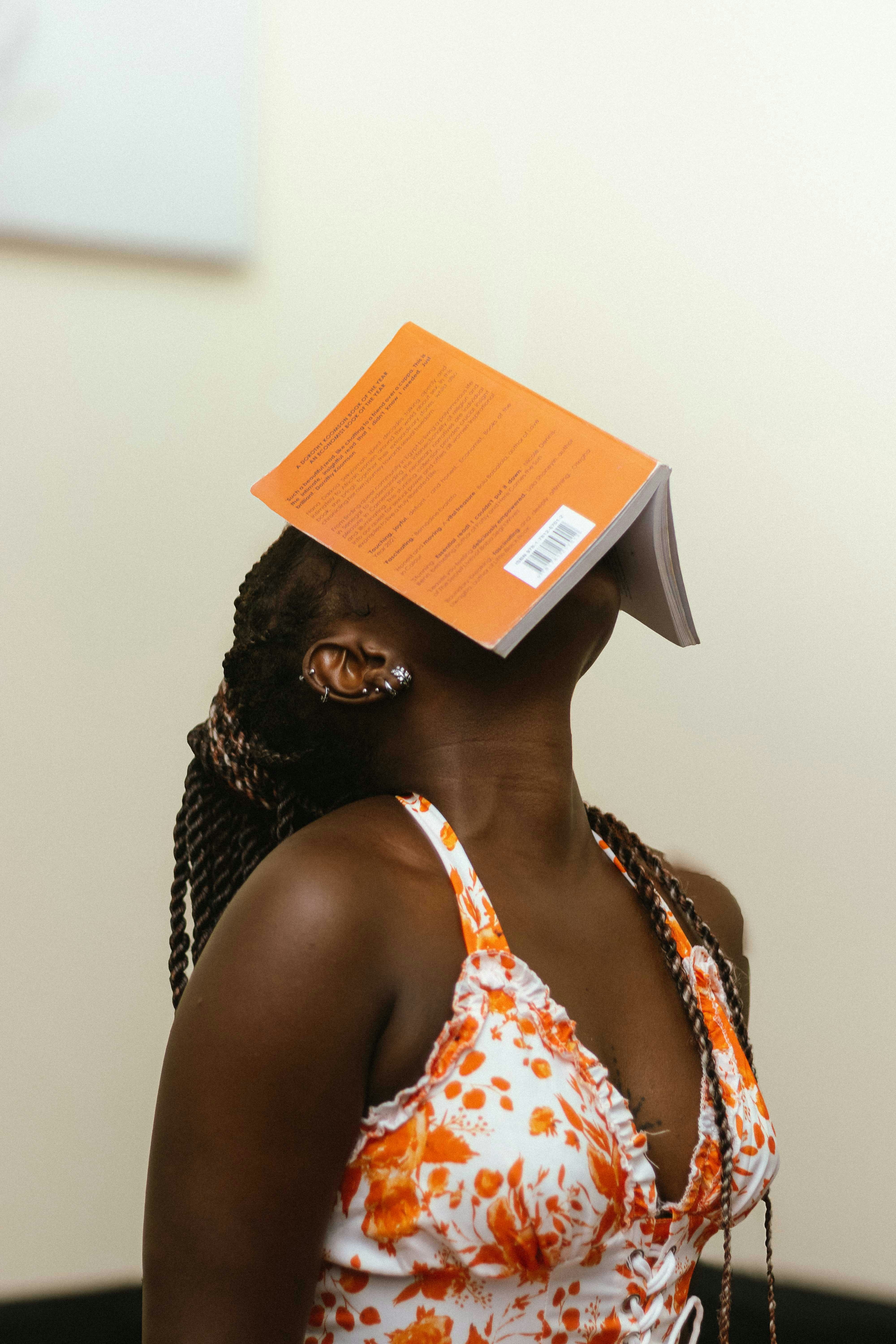 A woman with braided hair balancing an orange book on her face
