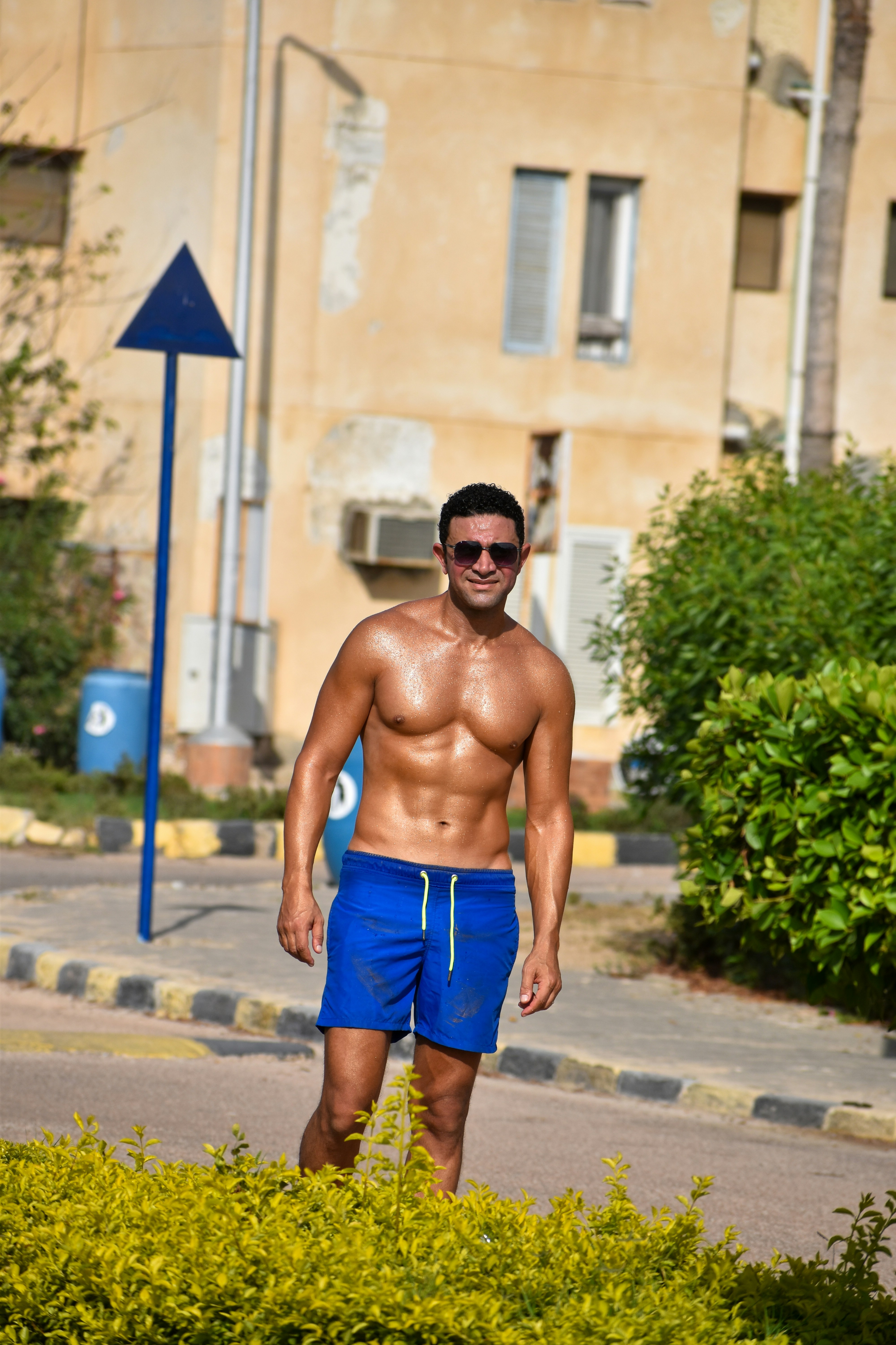 A shirtless man in blue swim trunks and sunglasses standing on a paved path