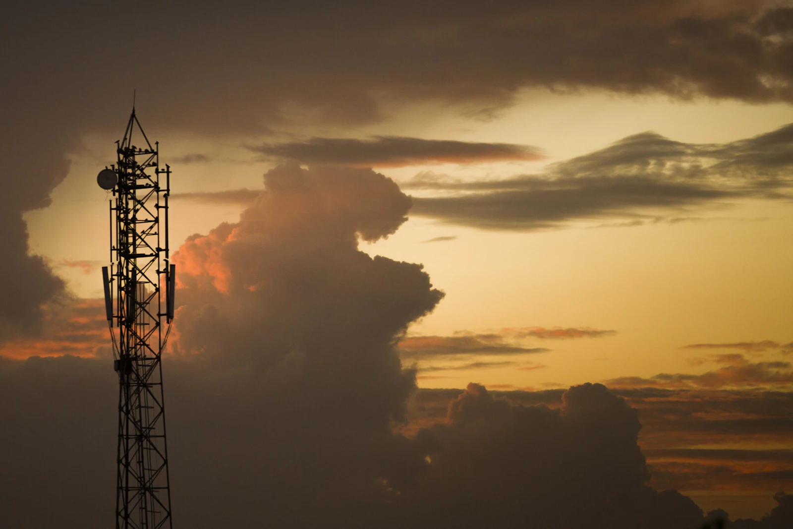 Telecommunications tower with 5G antennas silhouetted against golden hour clouds