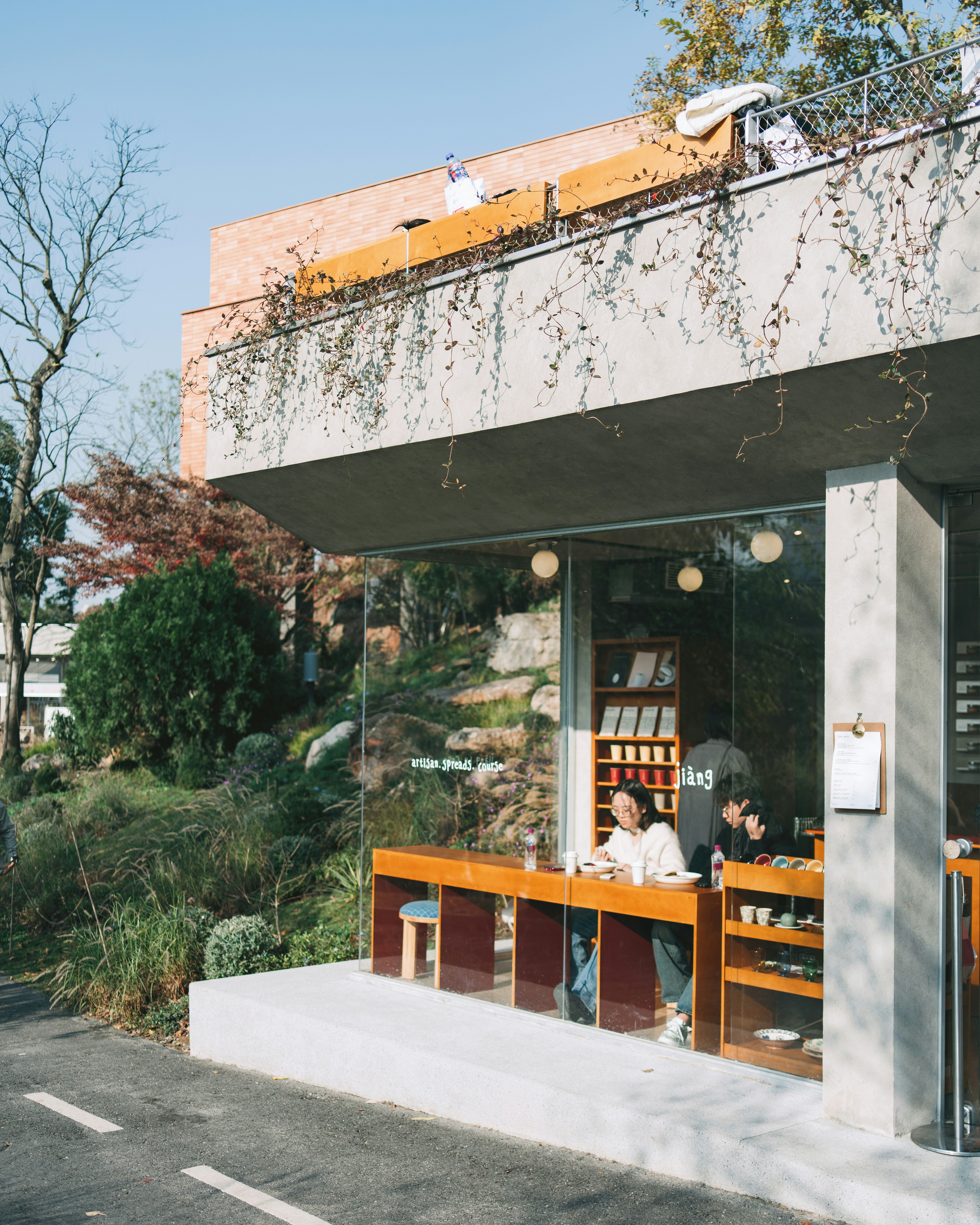 Two people sitting at a wooden counter inside a glass-walled cafe