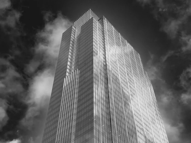 A black and white low angle view of a glass skyscraper against cloudy skies