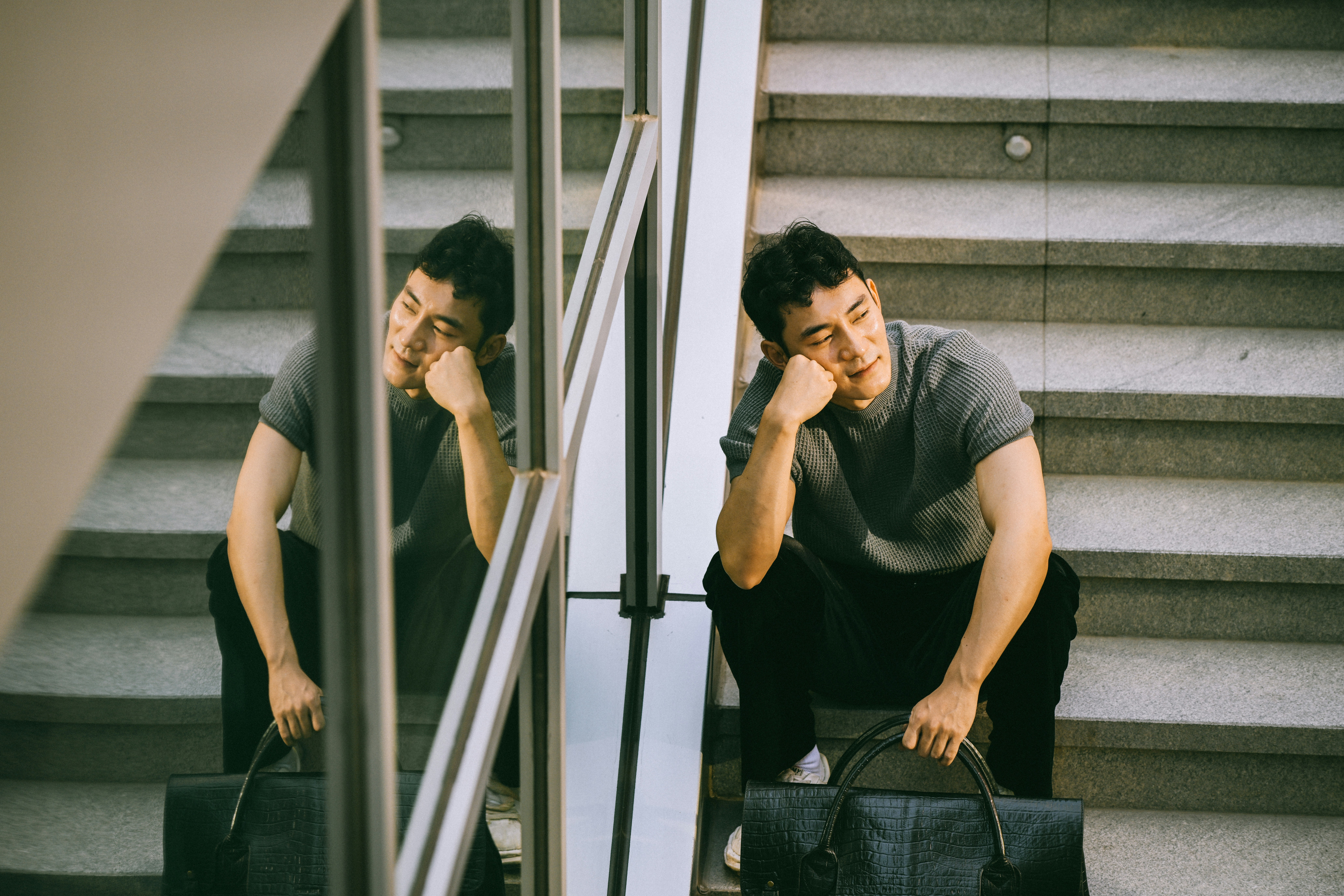 A man in a grey t-shirt holding a black bag on stone stairs