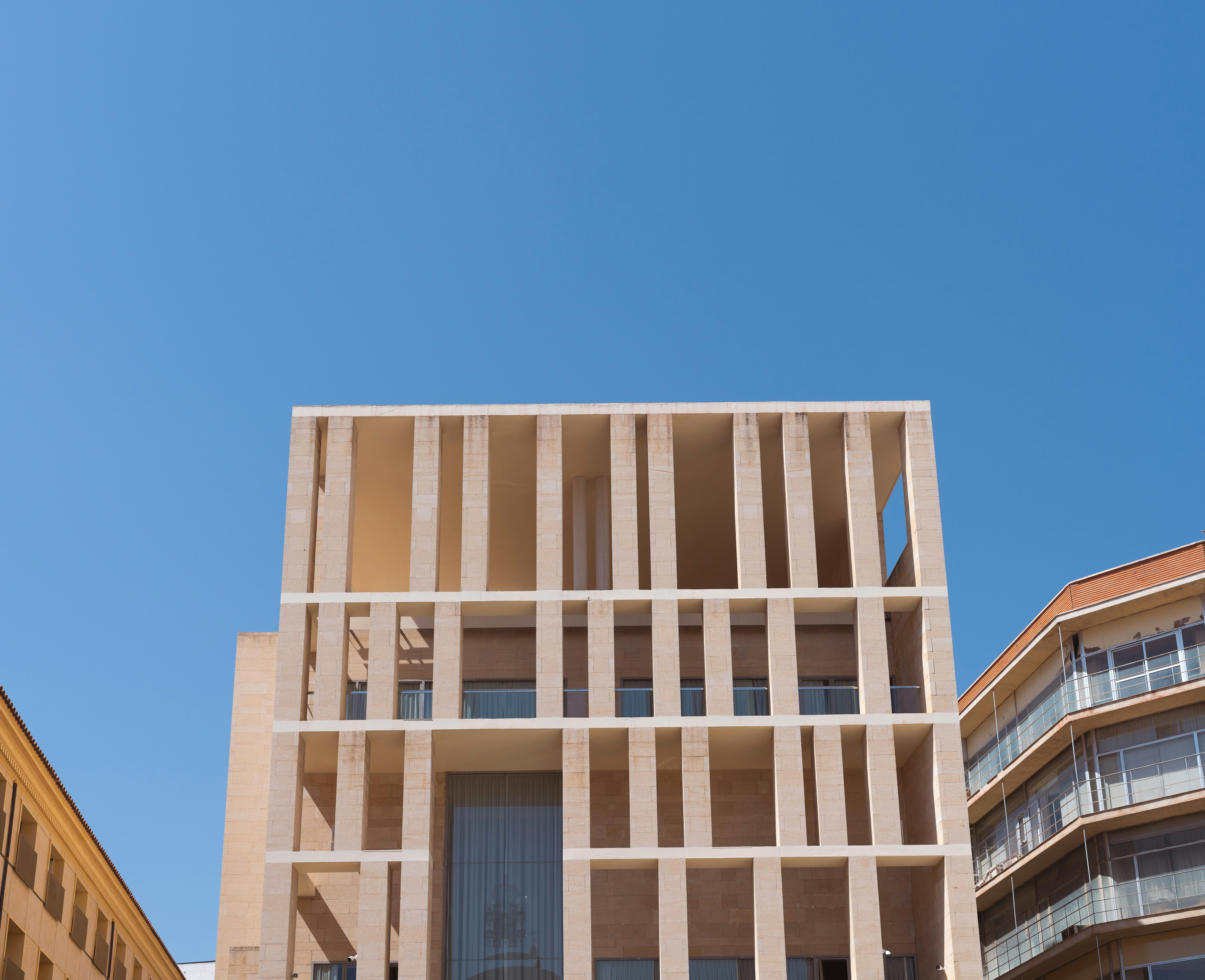 Modern building with a grid of stone pillars against a clear blue sky