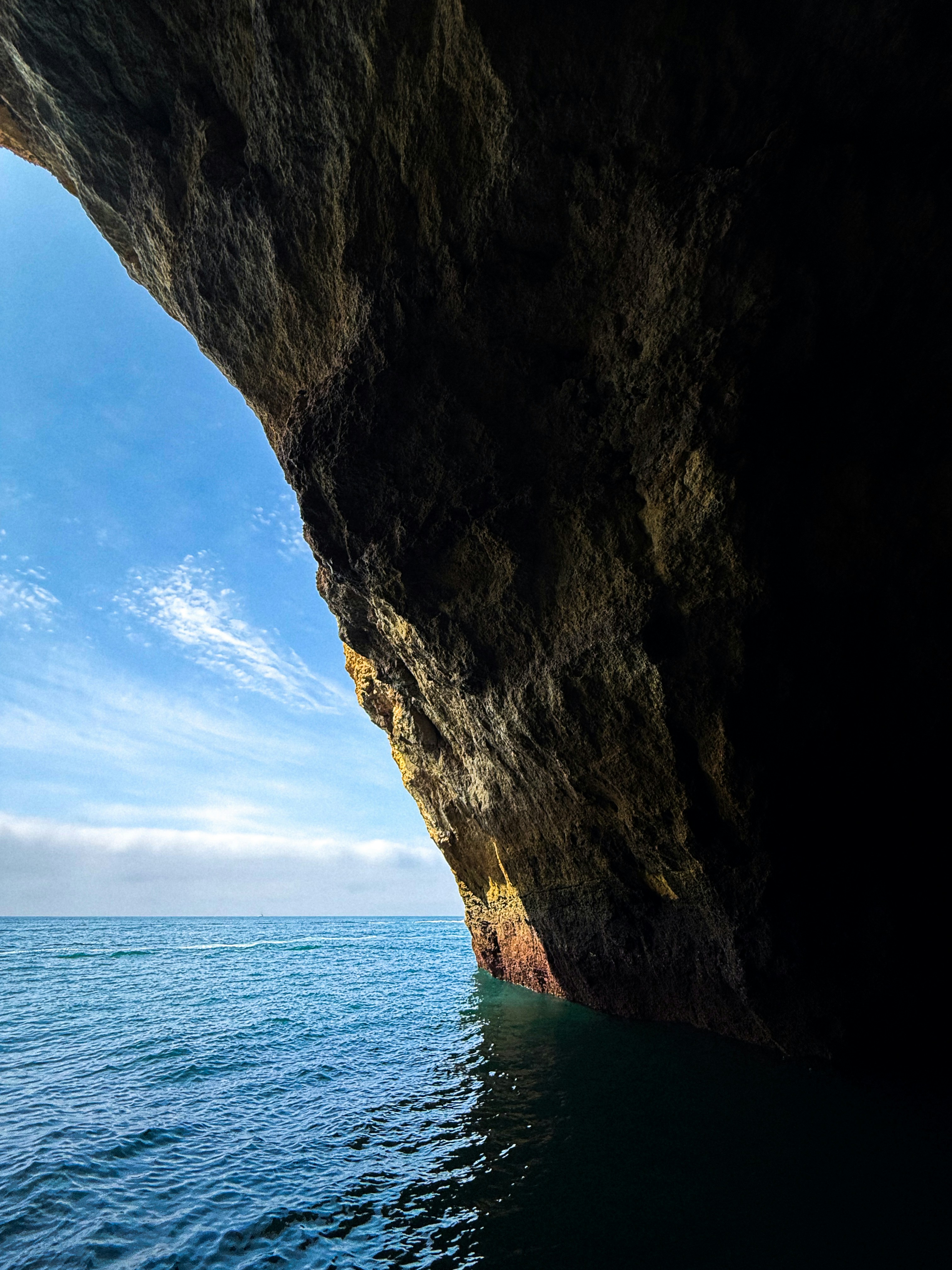 A dark rocky sea cave opening to a bright blue ocean and sky