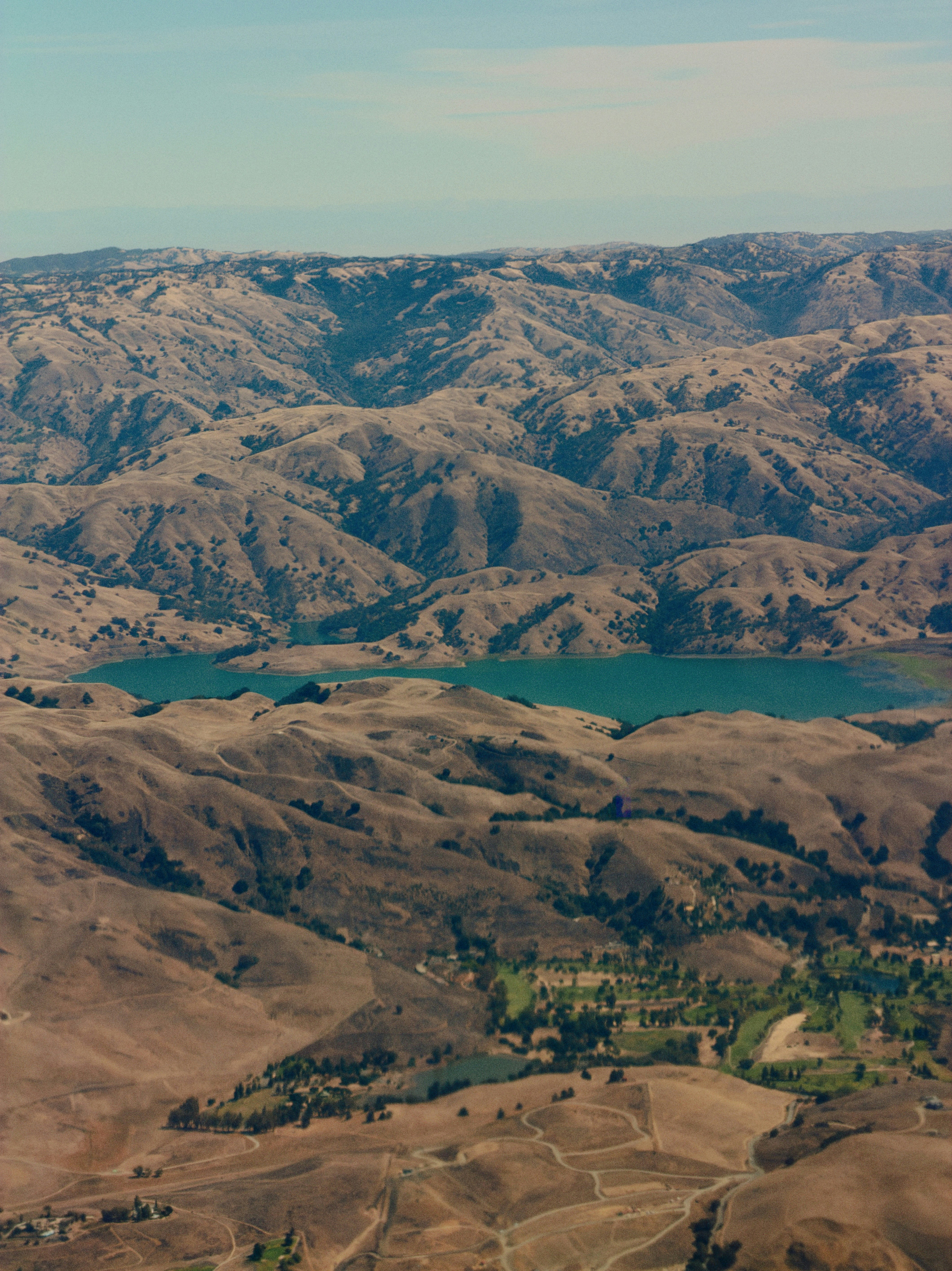 Vue aérienne d’un réservoir turquoise entouré de collines sèches et ondulantes
