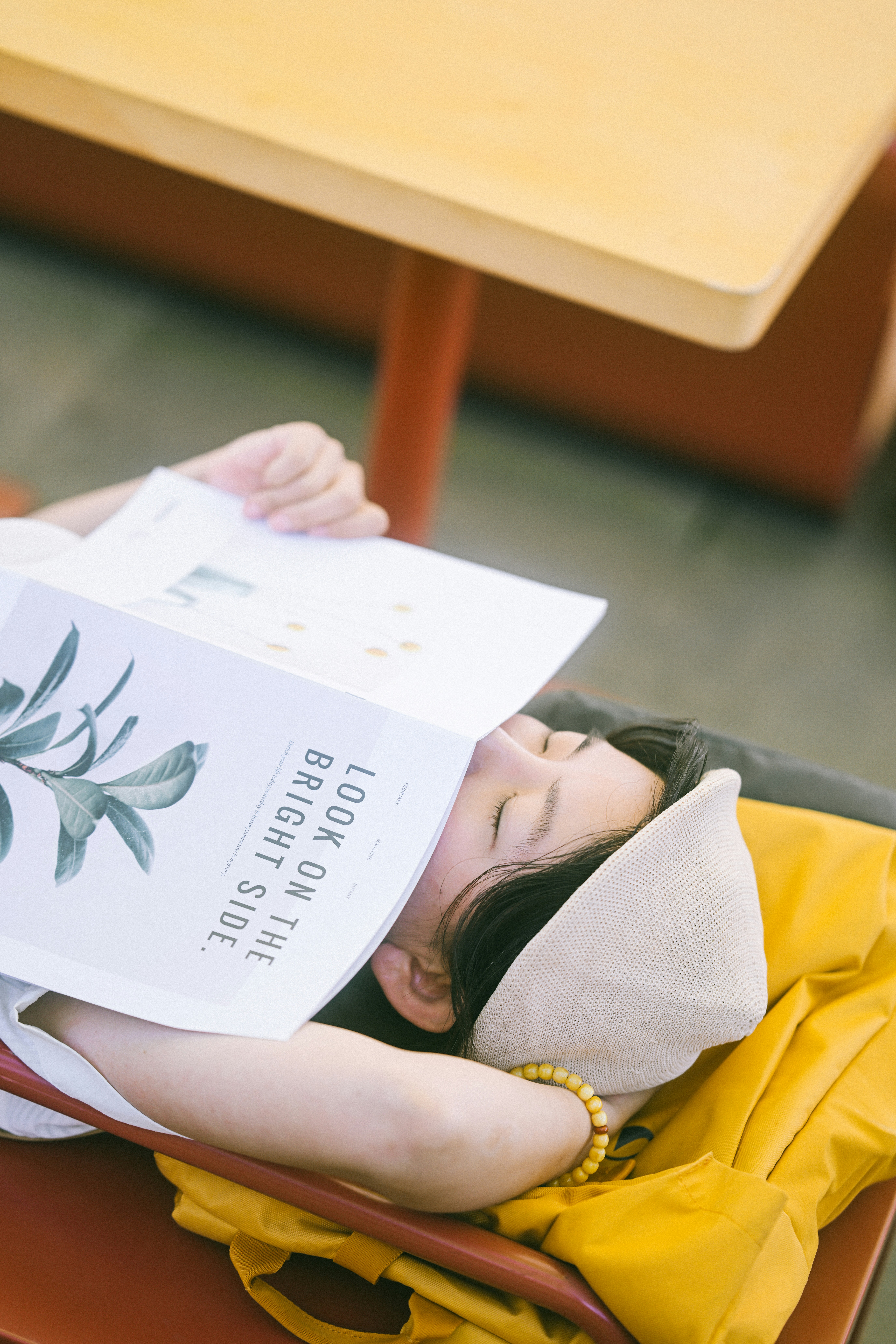A person wearing a beige cap resting with a magazine covering their face