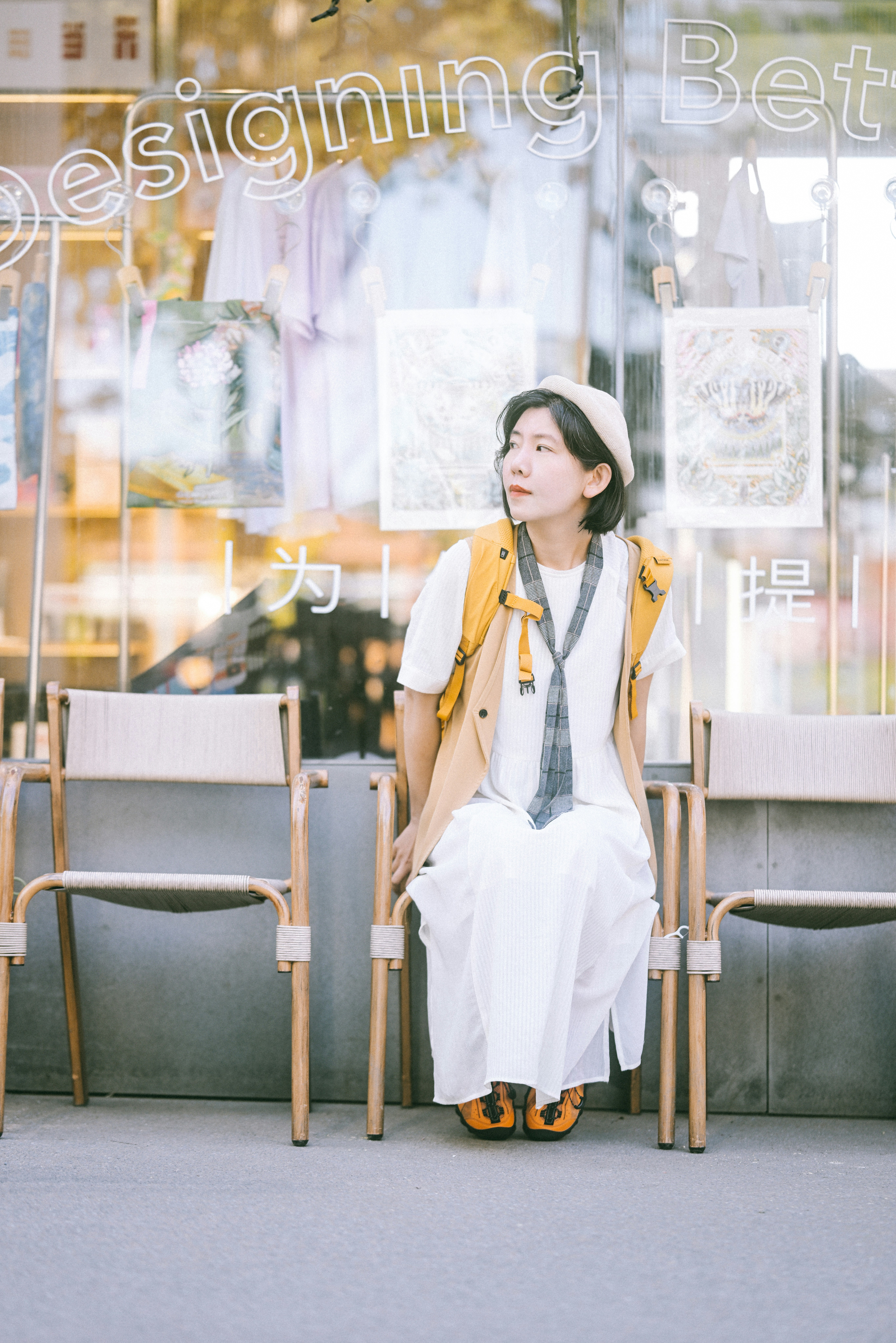 A woman in a white dress and tan vest sitting on a wooden chair