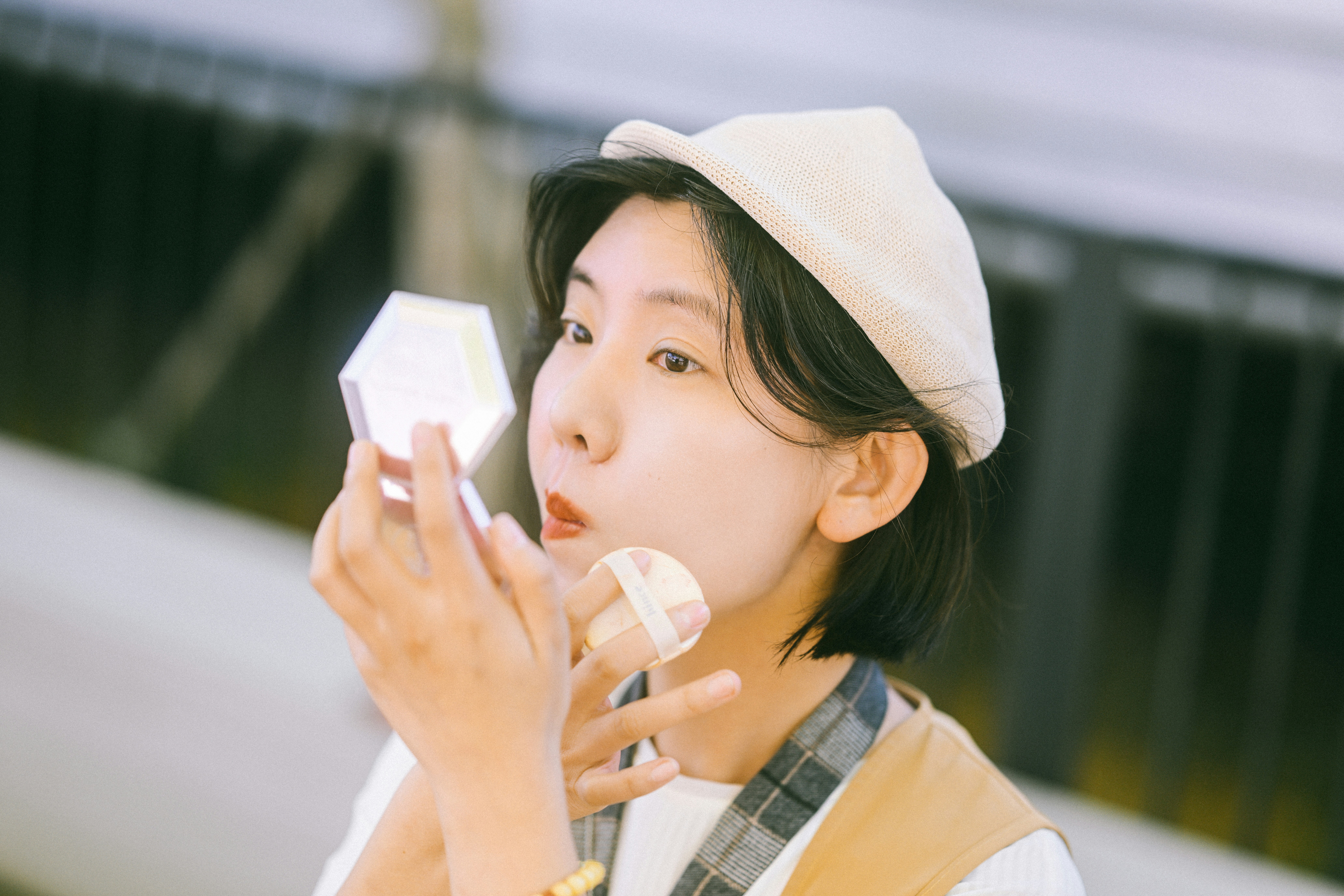 A woman in a beret applying makeup with a powder puff and mirror