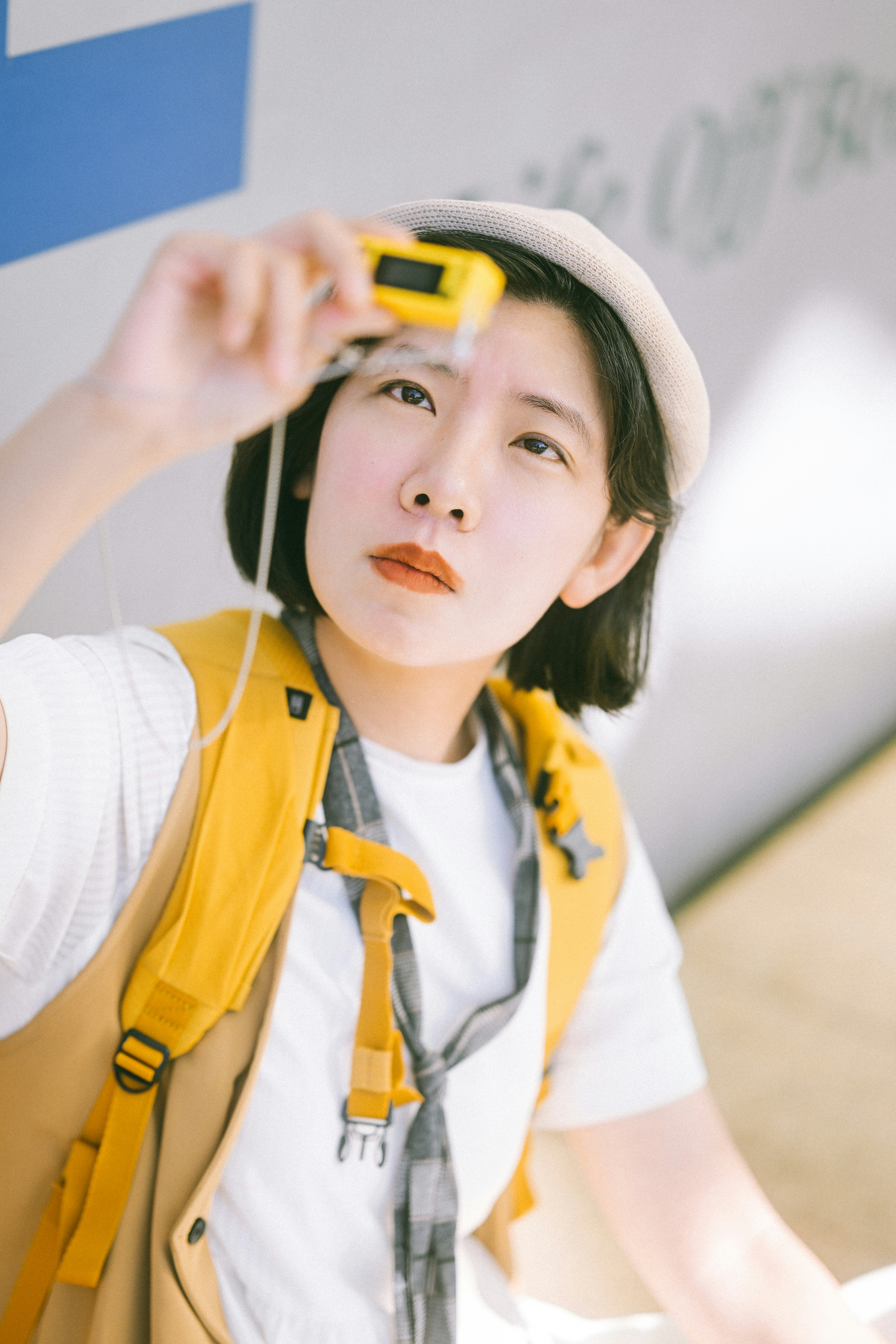 A person in a white shirt and yellow backpack looking through a small camera