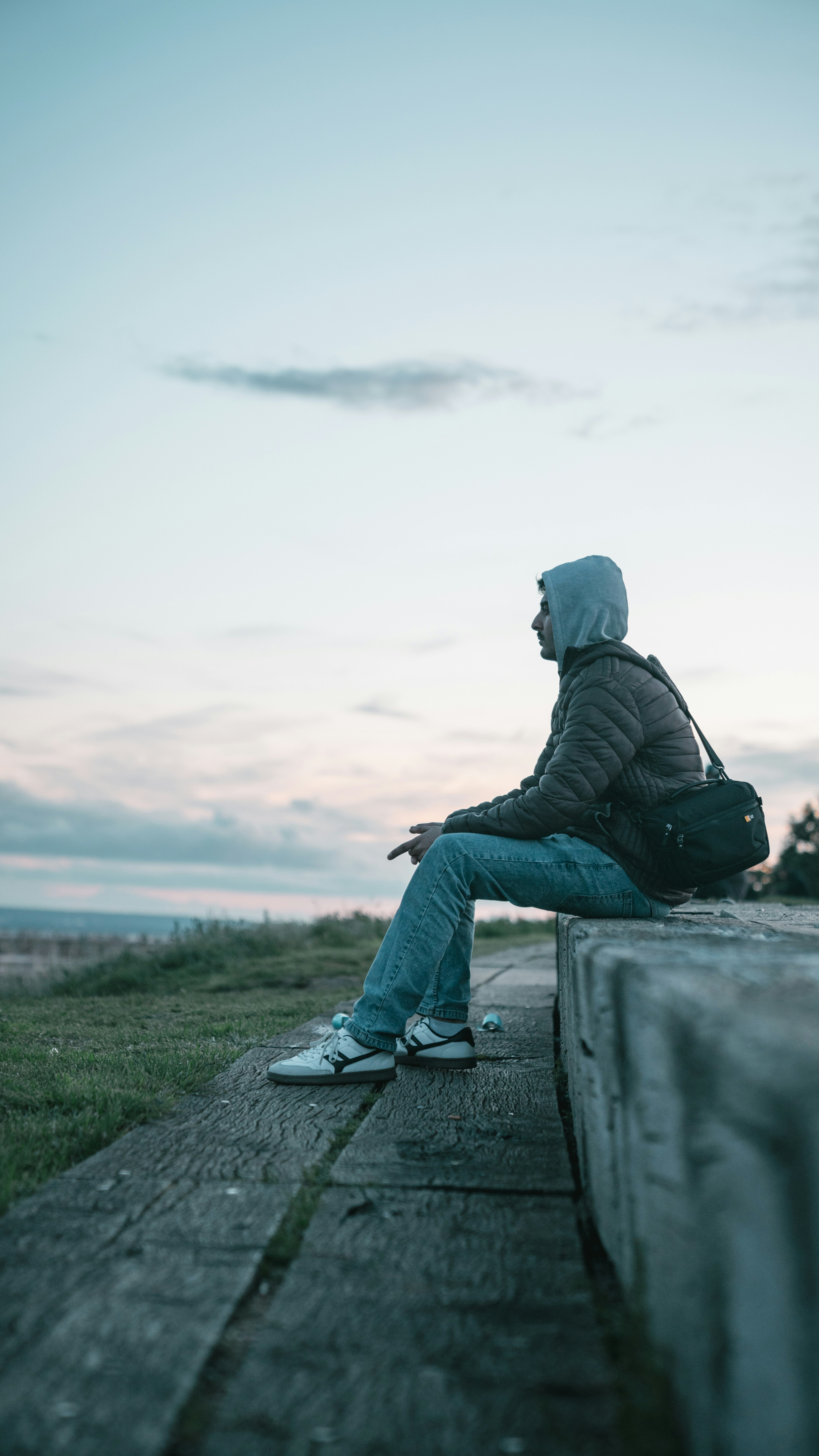 Eine Person in grauem Hoodie und Jacke sitzt auf einer Betonkante