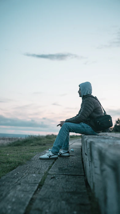 A person in a grey hoodie and jacket sitting on a concrete ledge
