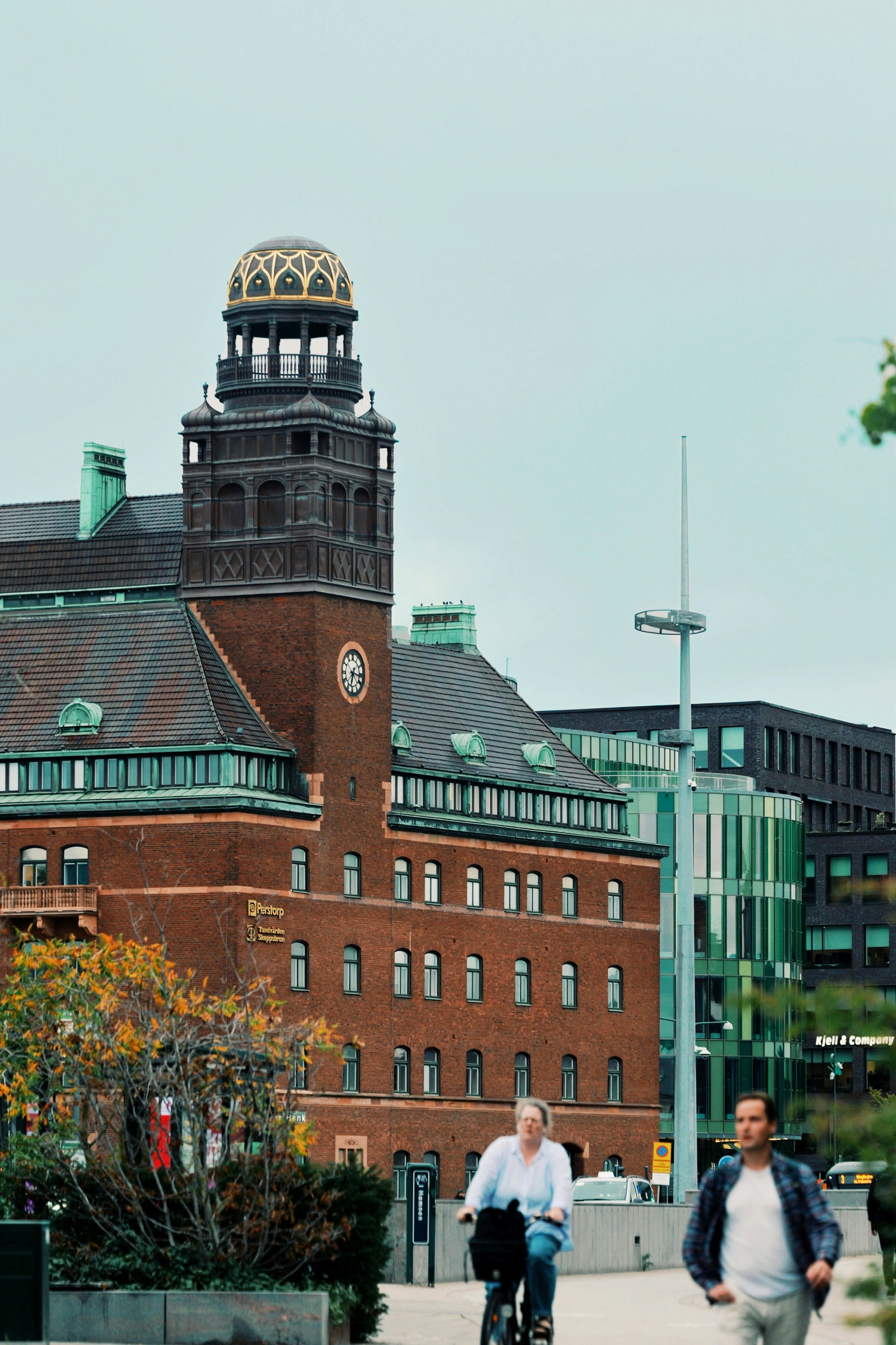 A person cycling past a historic brick building with a domed tower in Malmö