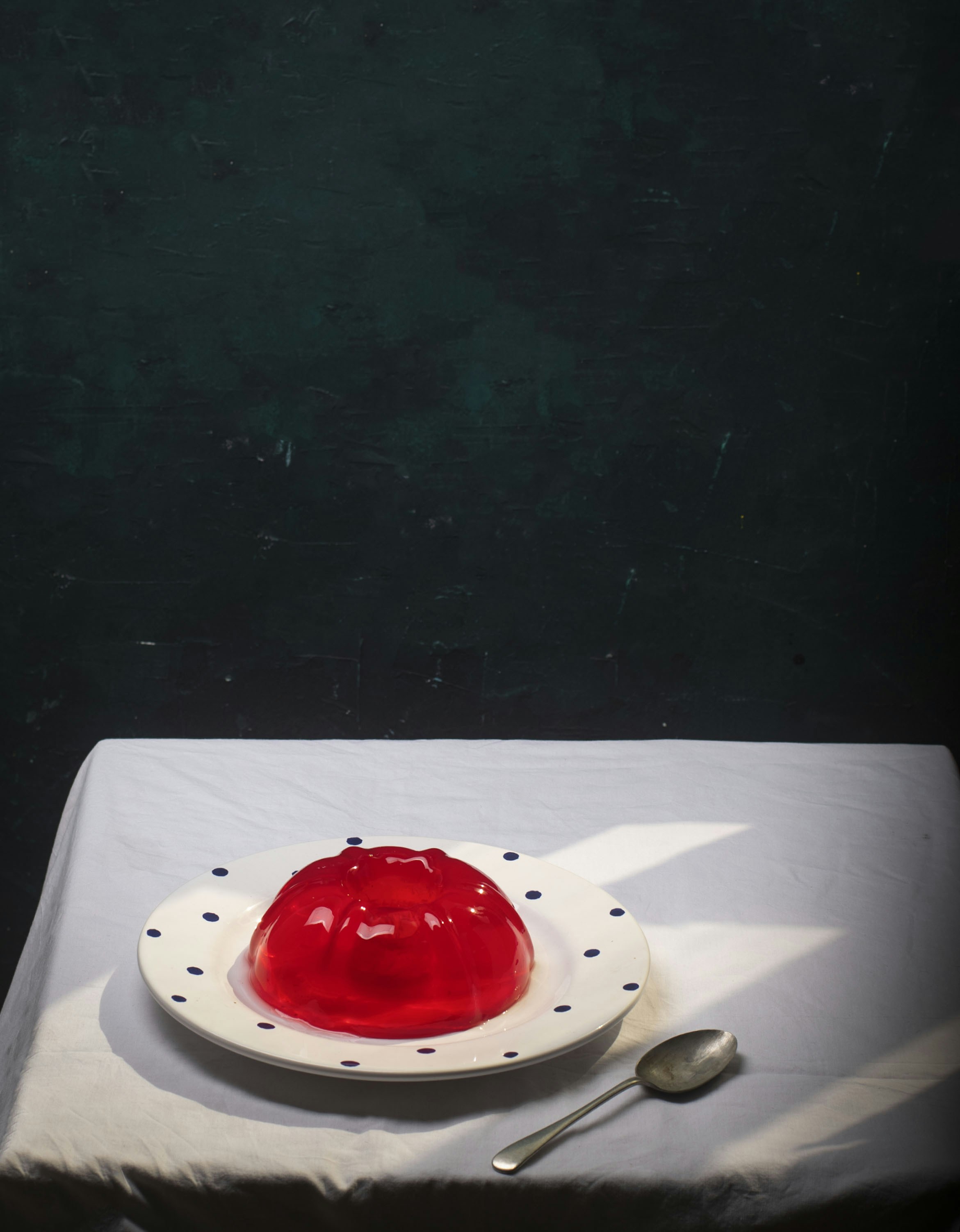A red gelatin mold on a polka dot plate with a silver spoon