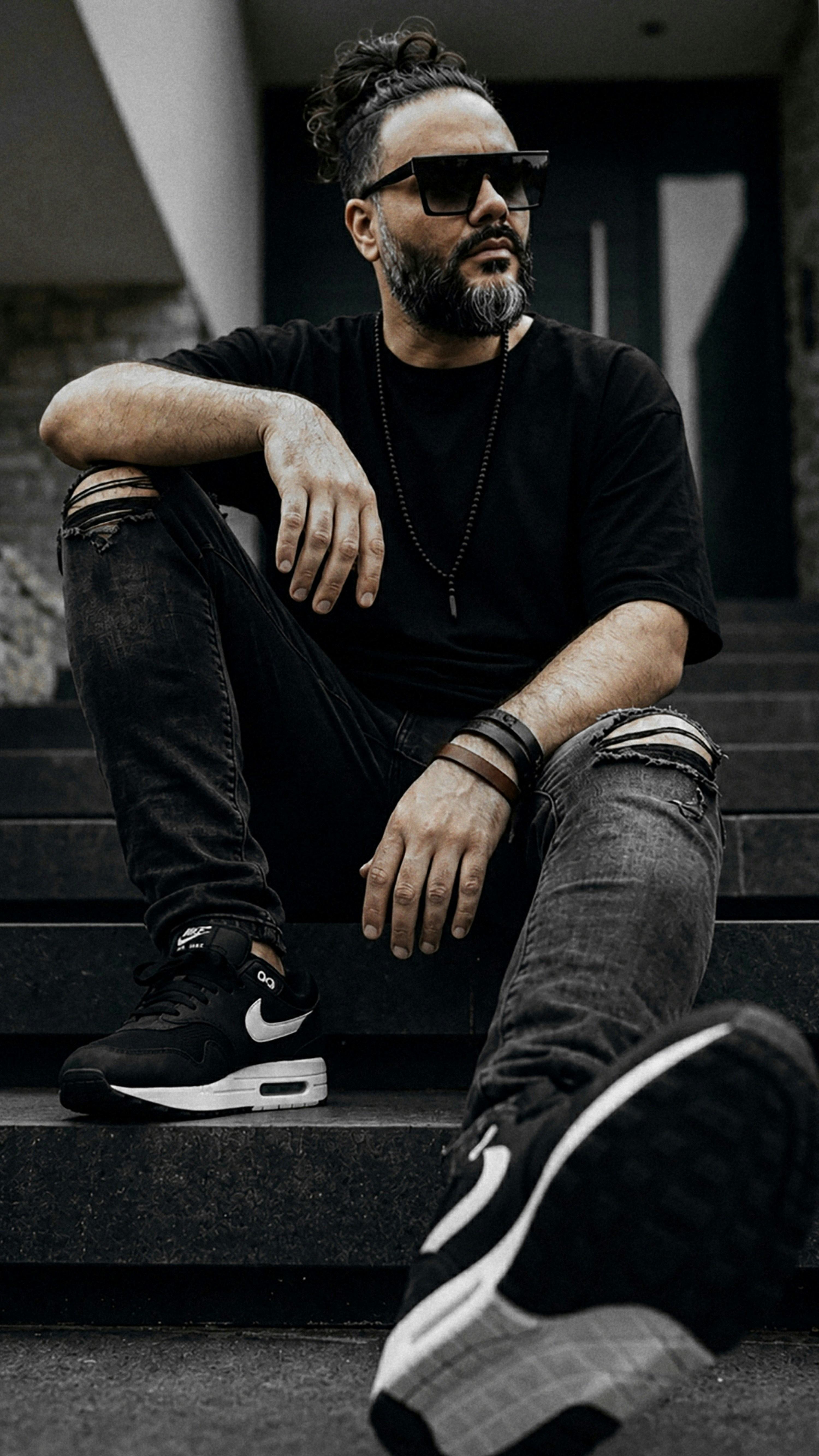 A man with a beard and hair in a bun wearing sunglasses and ripped jeans