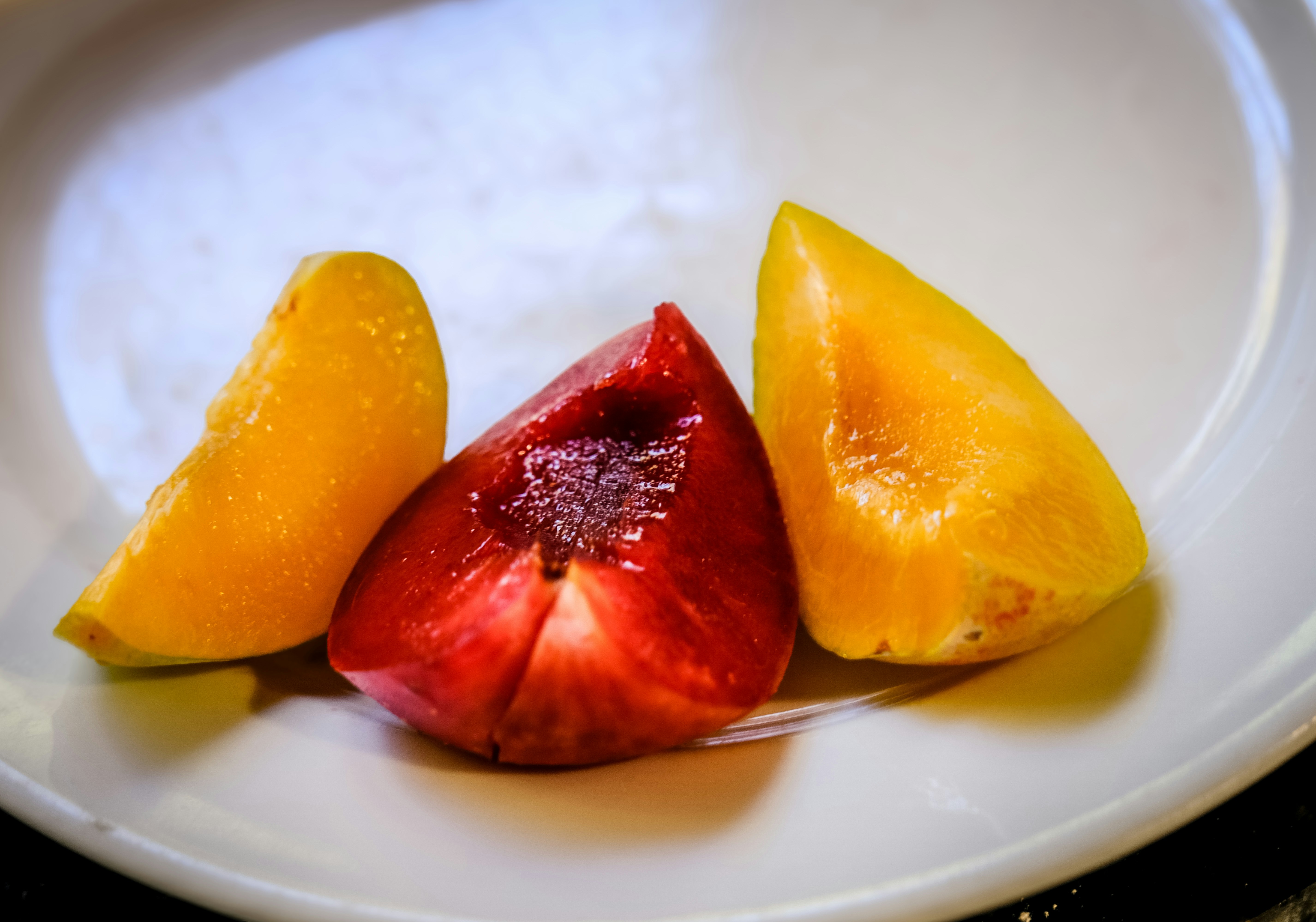 Two yellow peach slices and one red plum slice on a white plate