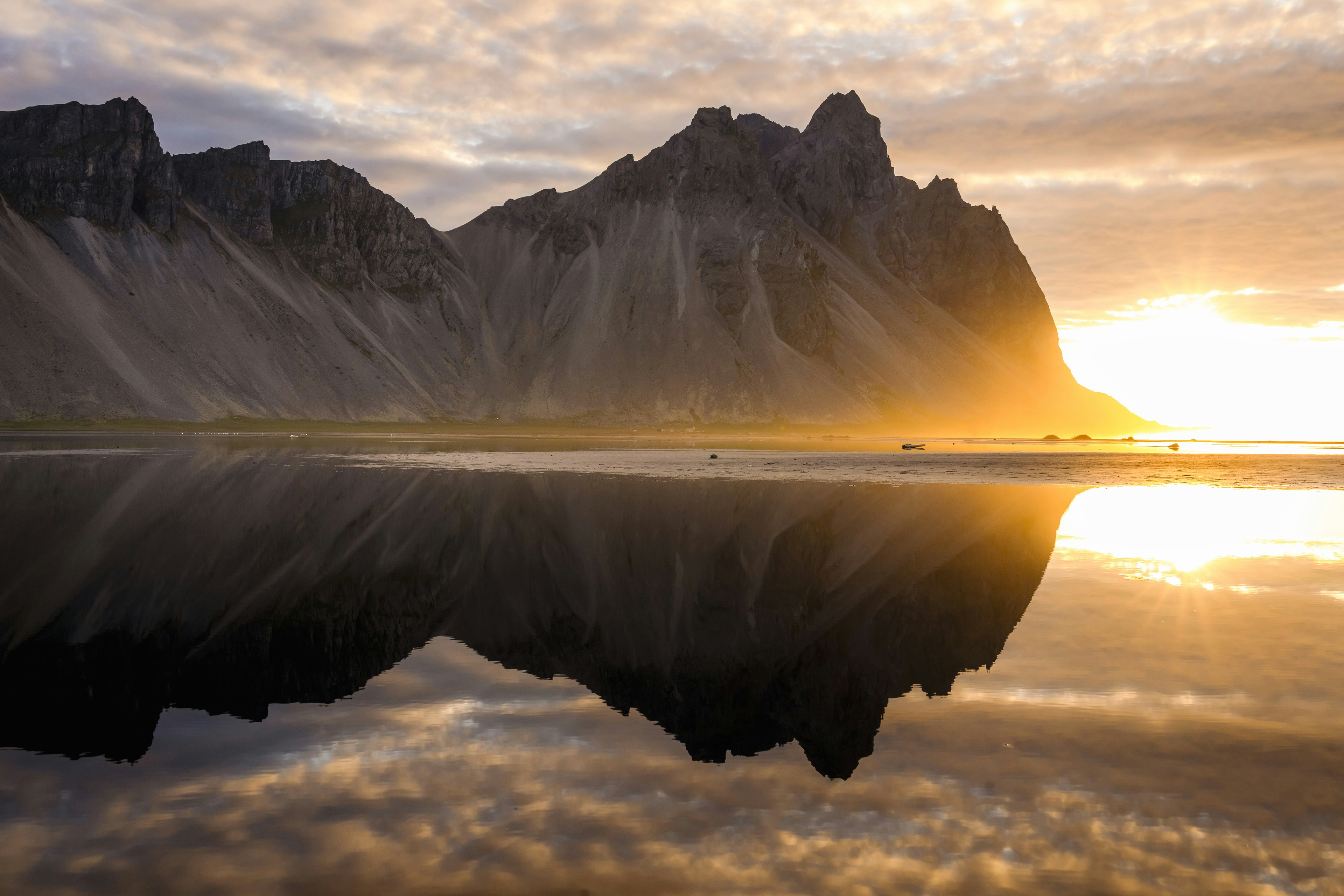 Vestrahorn mountain reflected in calm water under a warm golden hour sky