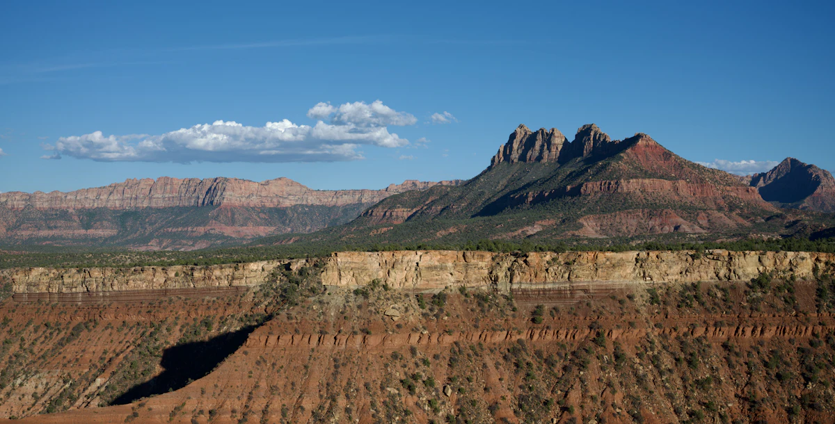 Red slopes and a pale cliff band seen from Gooseberry Mesa, with sandstone peaks behind