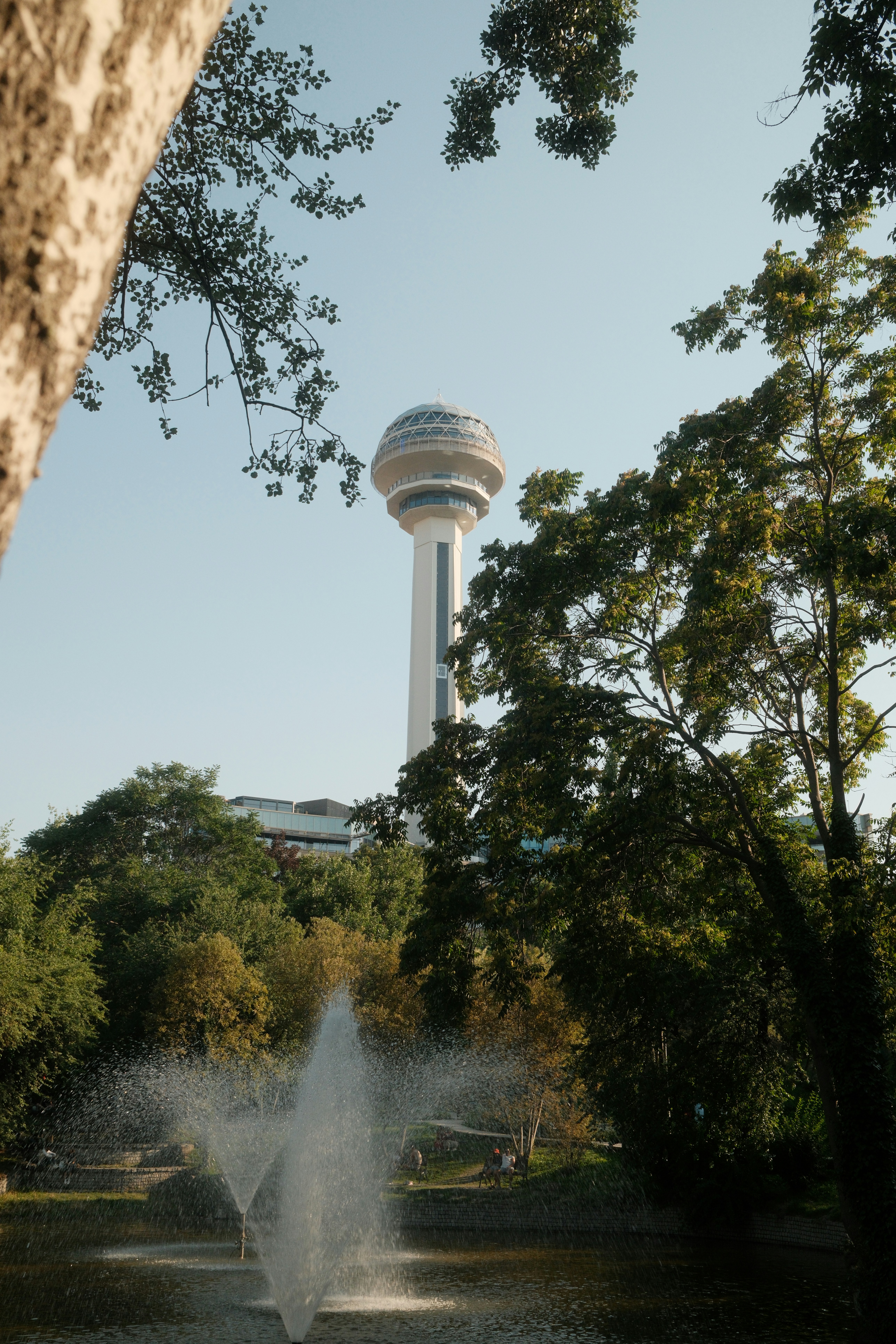 Atakule-Turm, der über üppig grünen Bäumen und einem Brunnen in Ankara emporragt