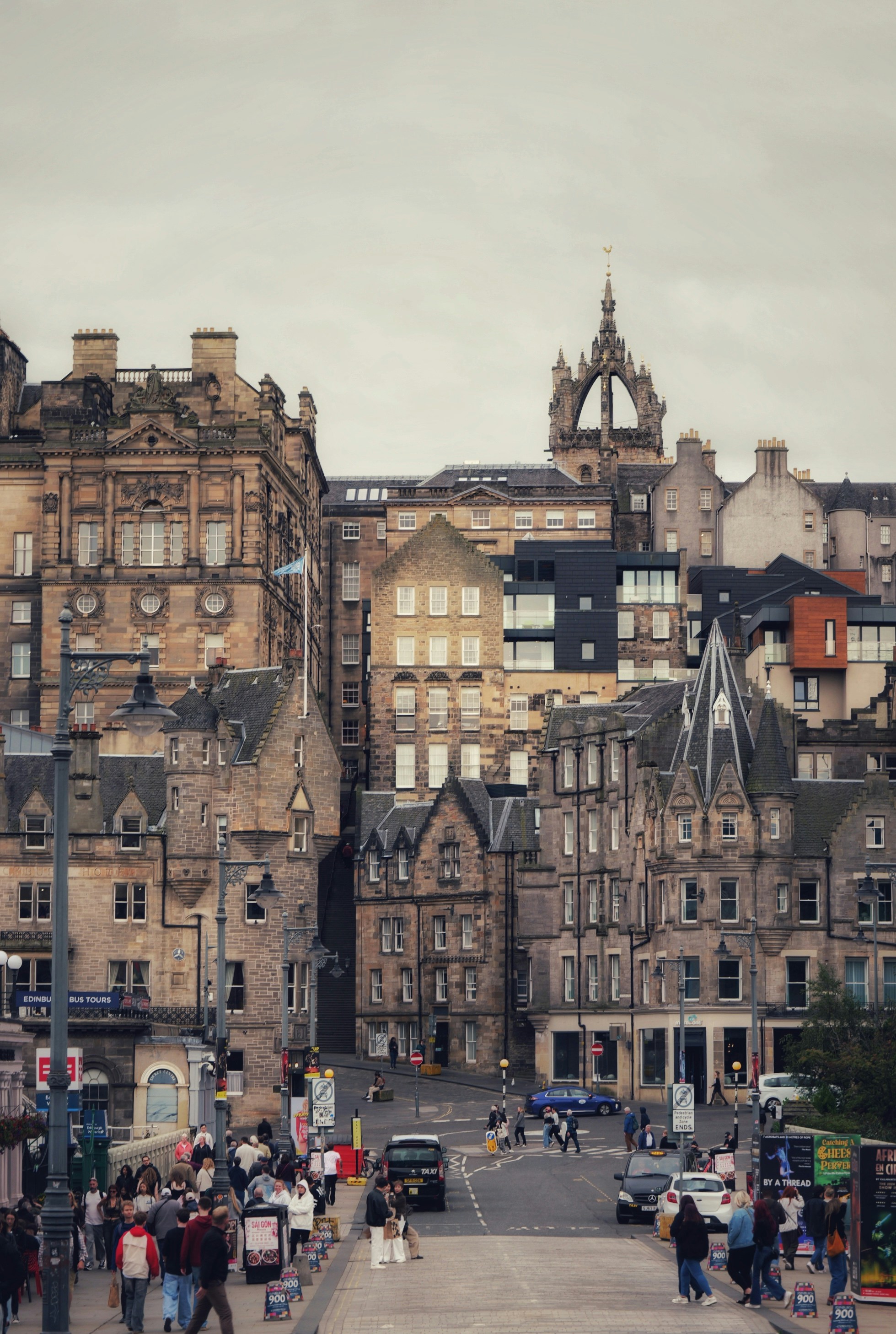 People walking on a street in Edinburgh with historic stone buildings and a church spire