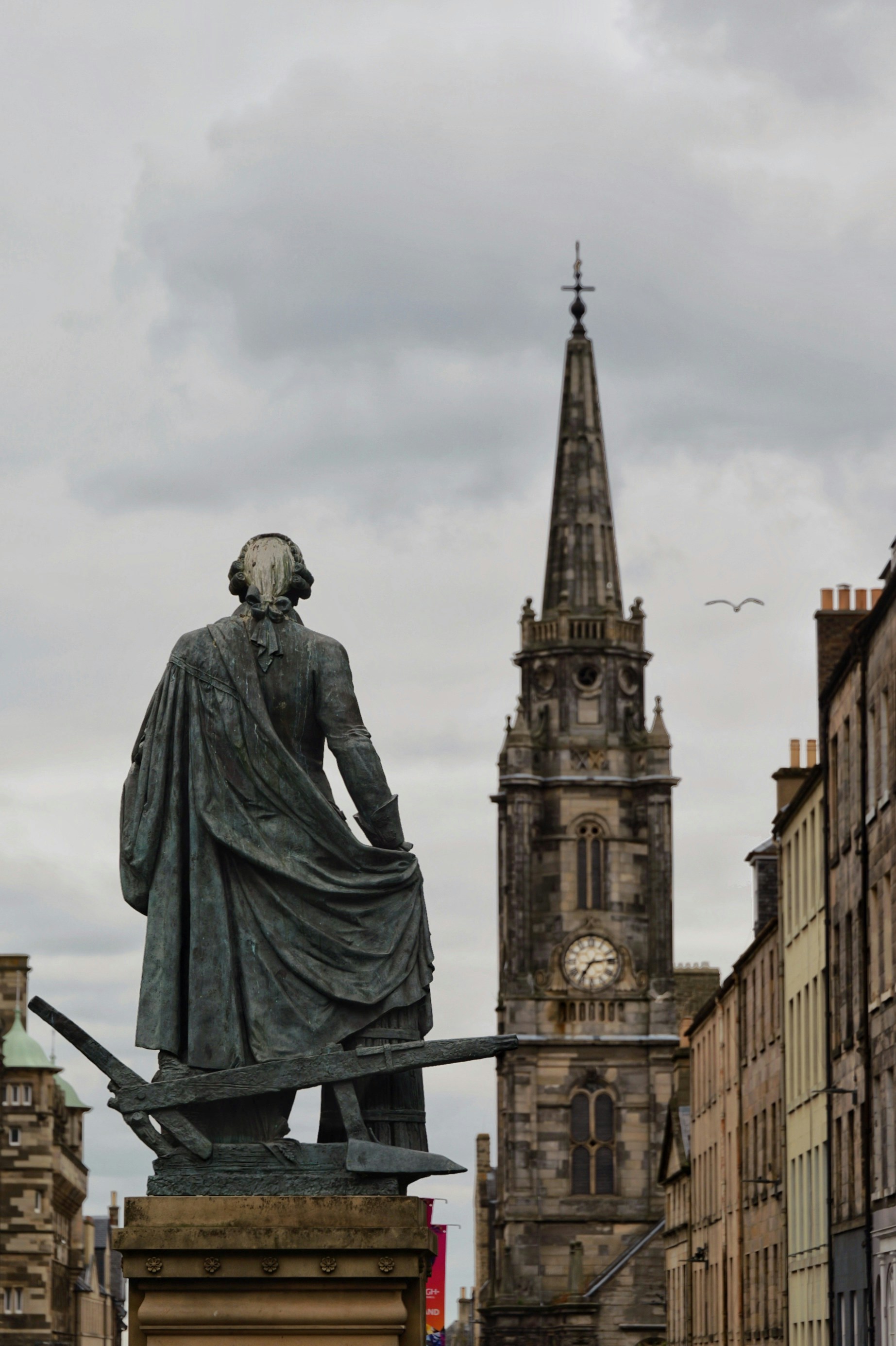 A bronze statue of a man in period clothing facing a stone church tower