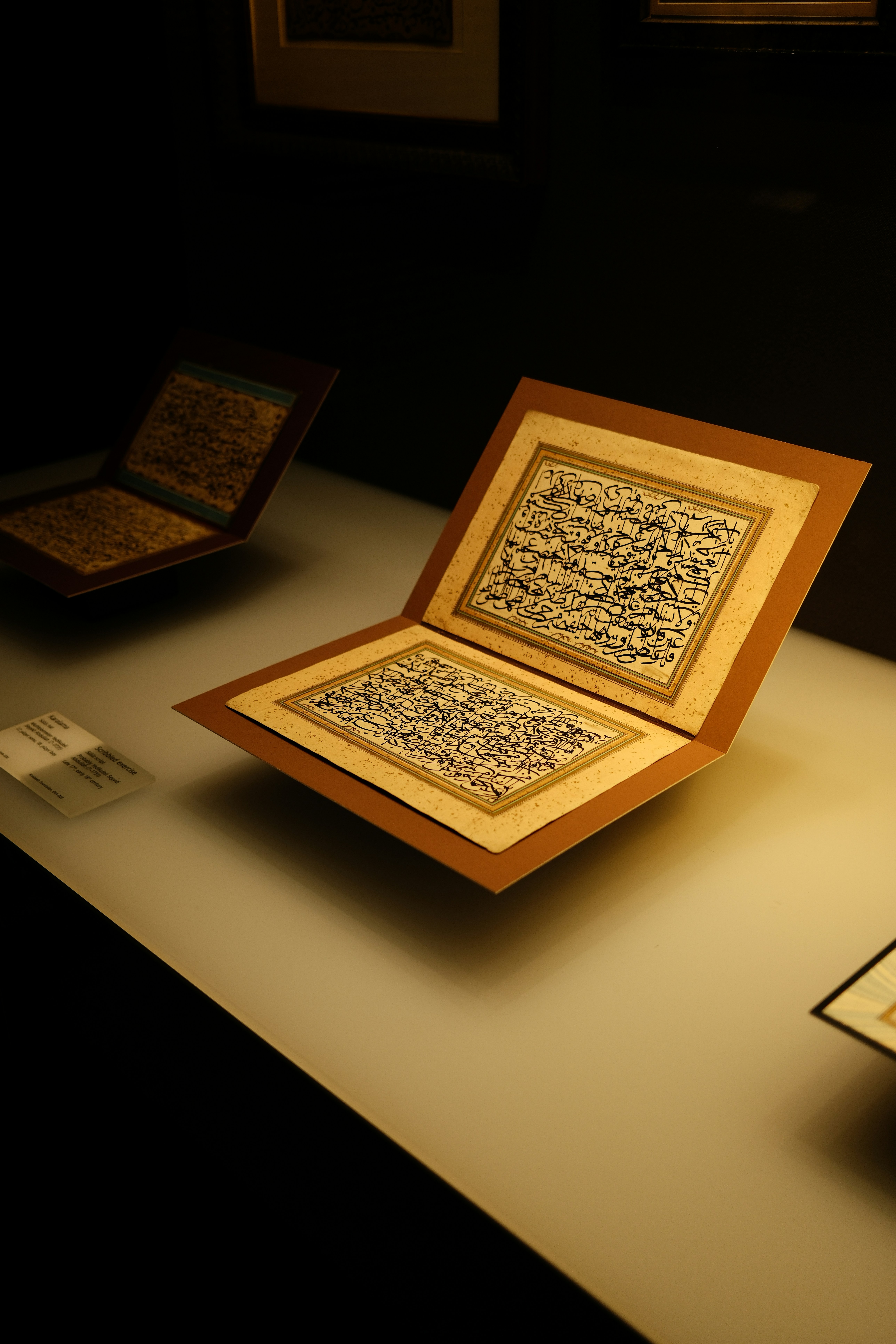 Ein offenes Manuskript mit kunstvoller schwarzer arabischer Kalligraphie auf einem beleuchteten Ausstellungsregal