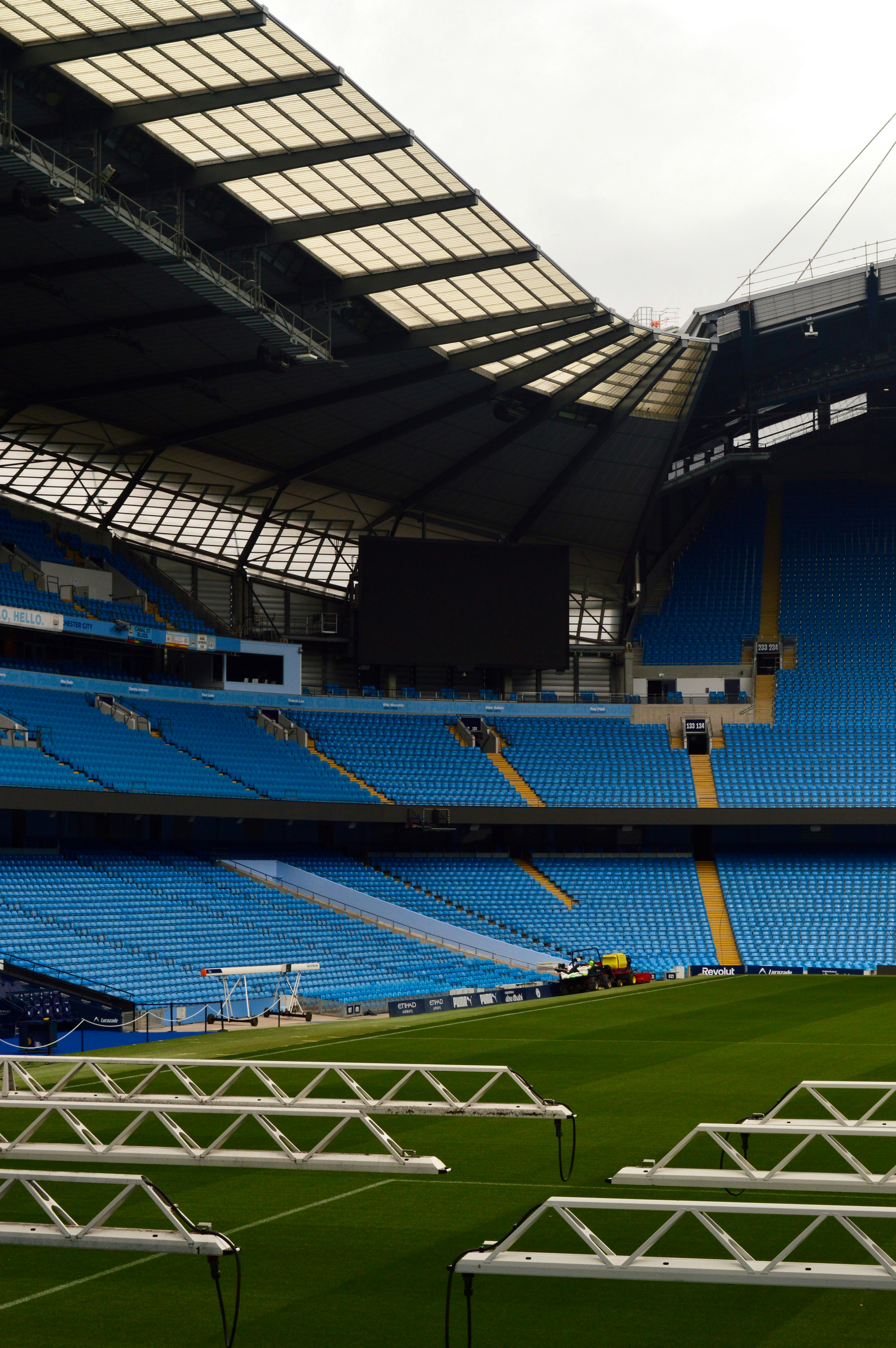 Rows of blue stadium seats overlooking a green pitch under a large roof