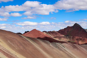 Red and brown striped mountains under a bright blue sky with white clouds