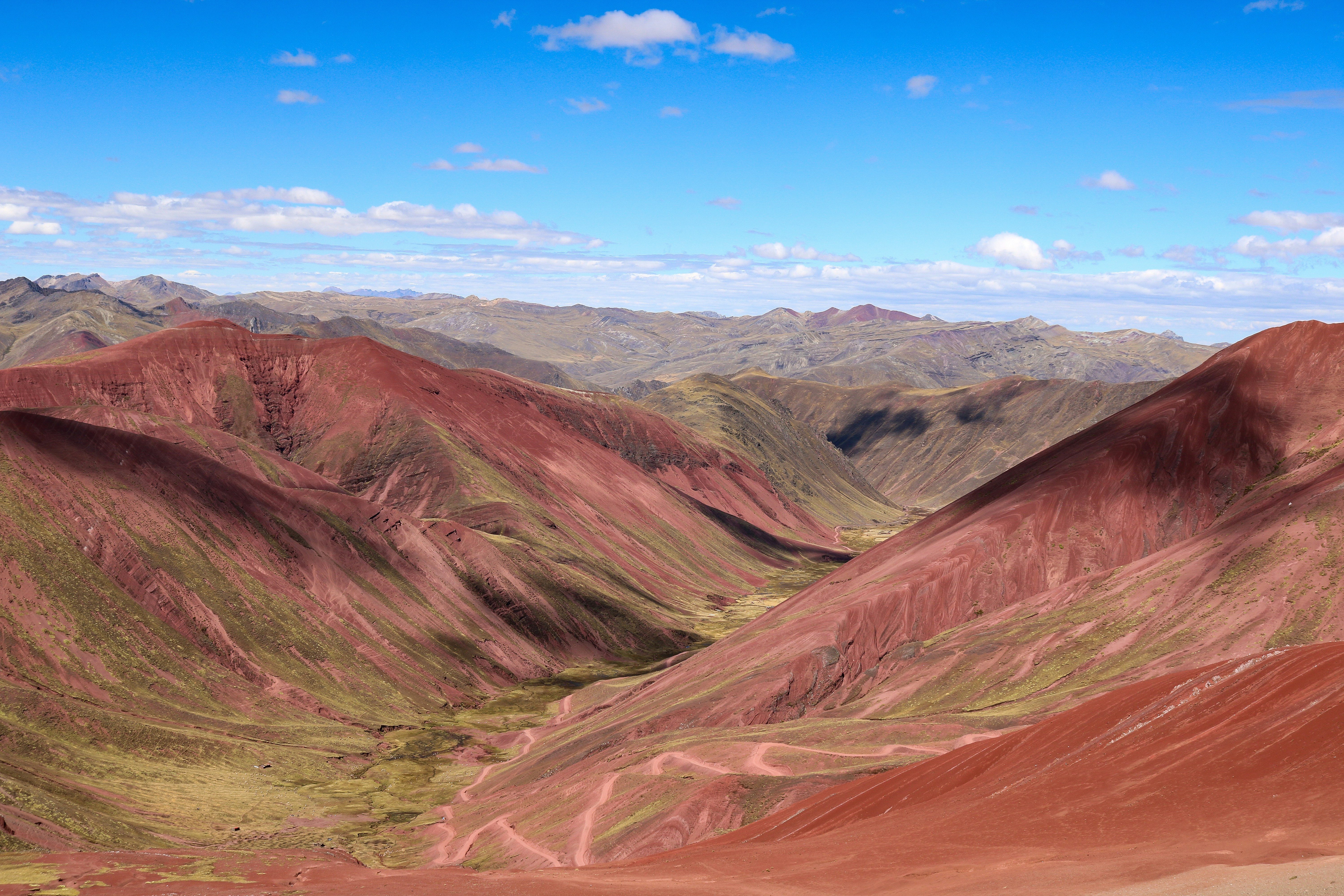 Red mountains and a winding dirt path in a deep valley under blue sky