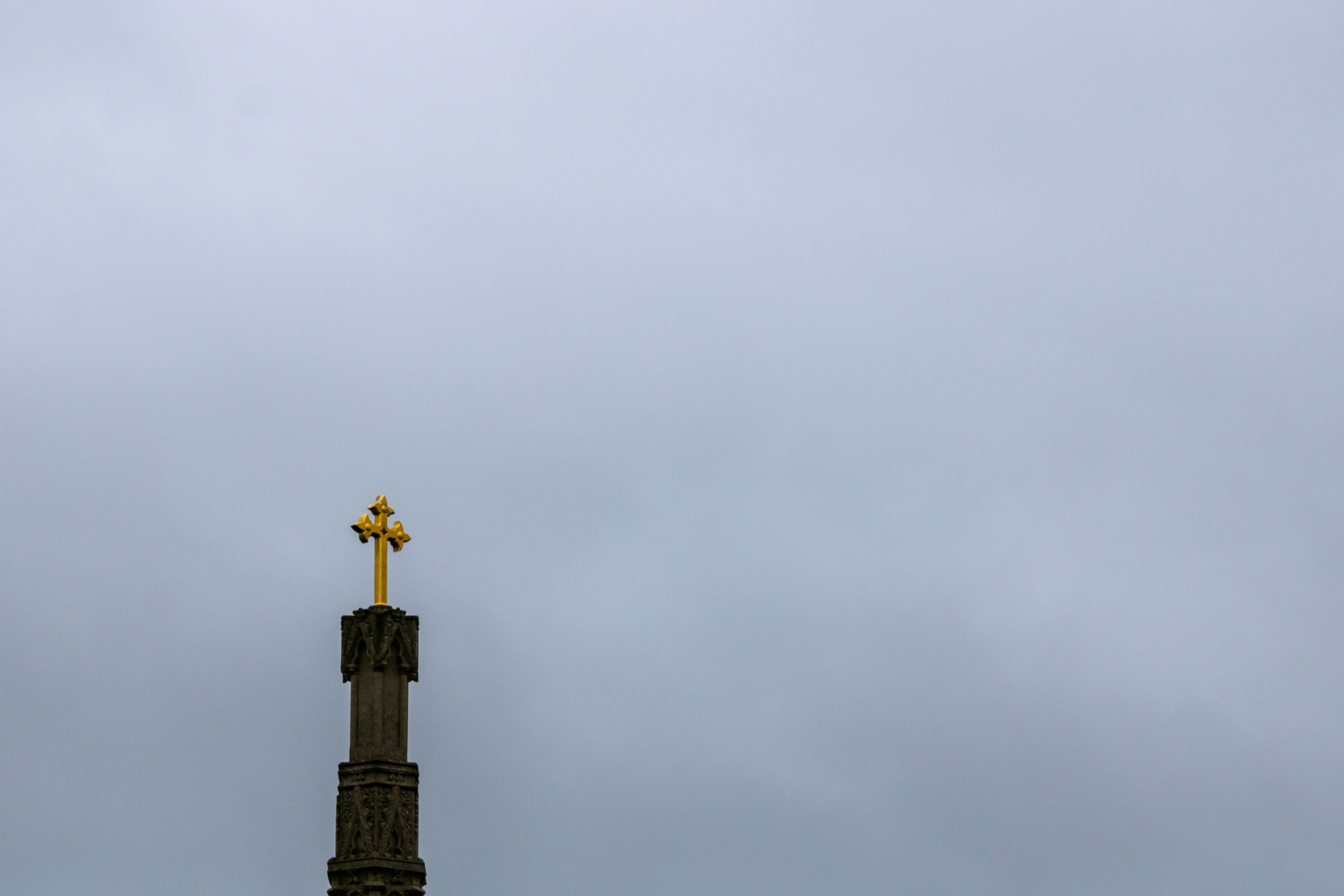 Una cruz dorada en lo alto de una aguja de piedra contra un cielo gris y nublado