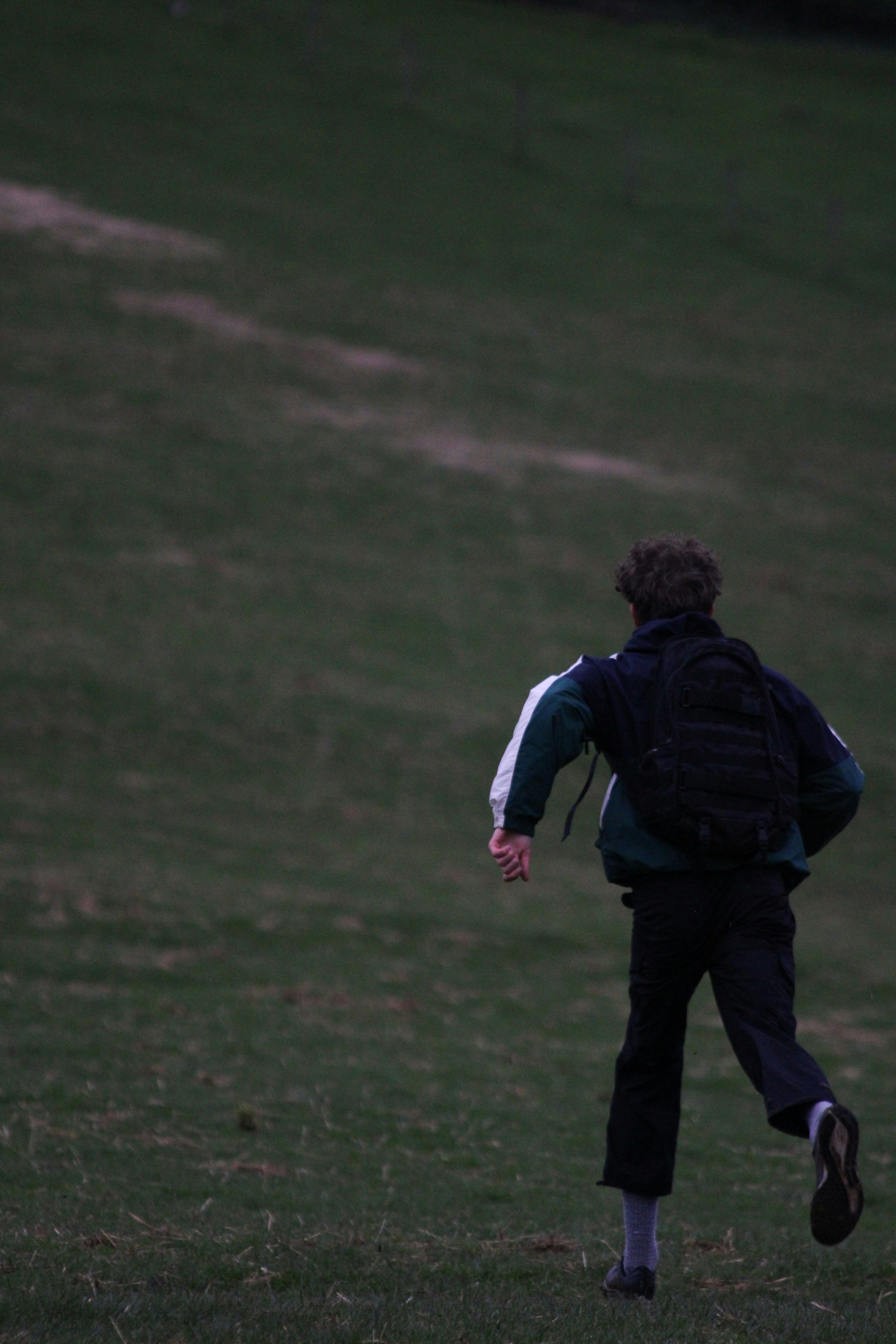 Una persona con mochila corriendo por un campo de hierba al anochecer