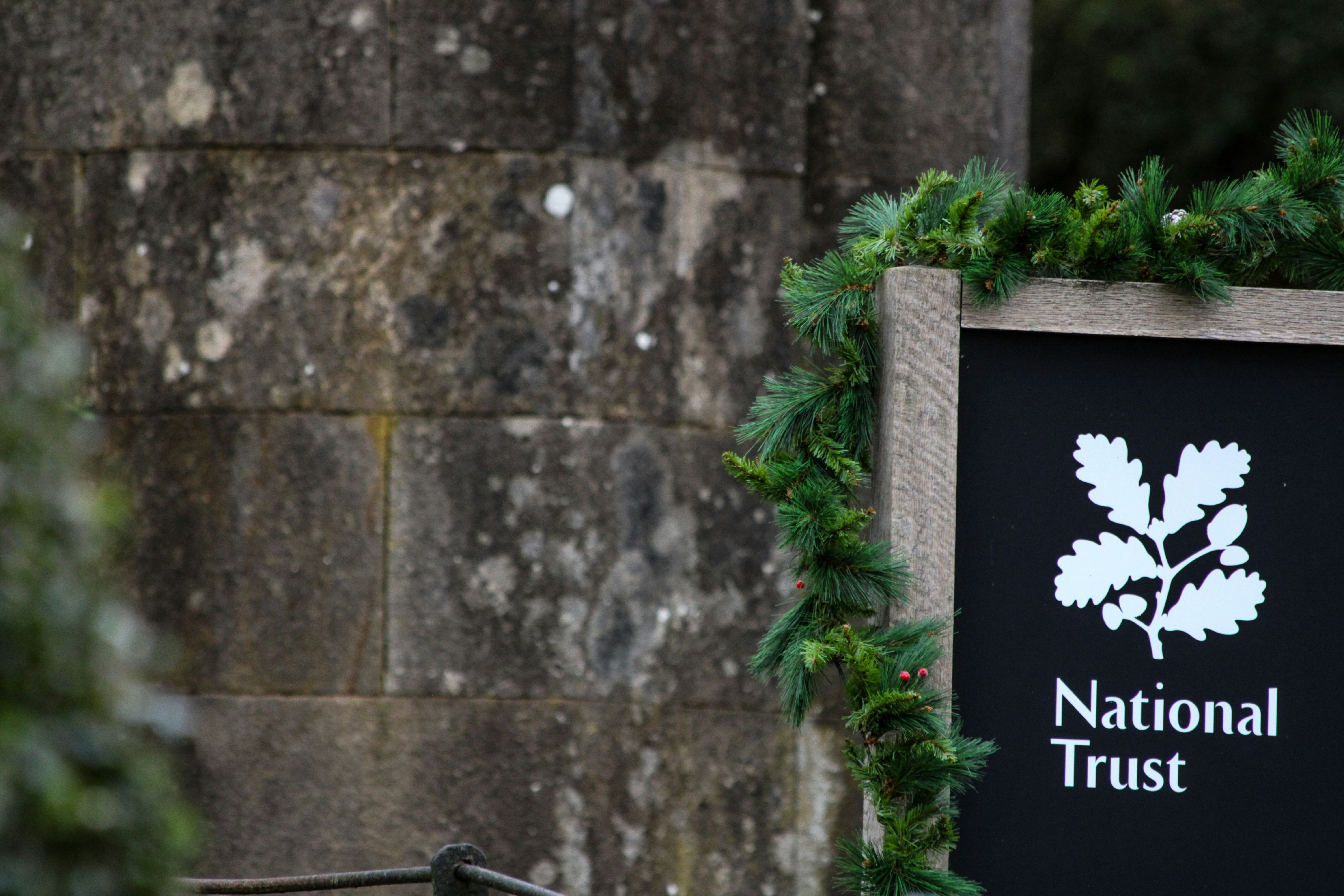 Un cartel del National Trust decorado con guirnaldas de pino contra un muro de piedra desgastado
