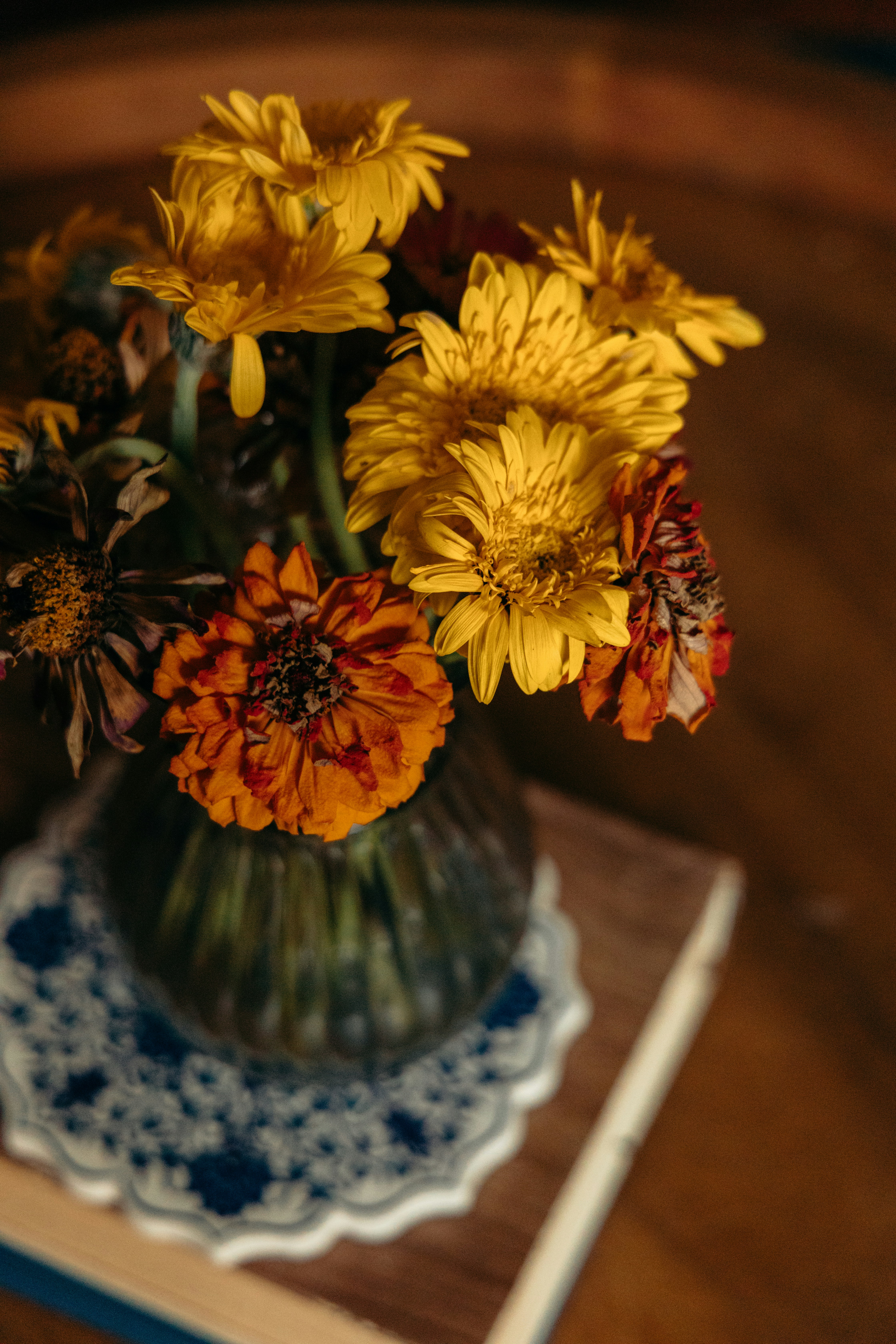 Gelbe und orangefarbene Blumen in einer Glasvase auf einem dekorativen Untersetzer