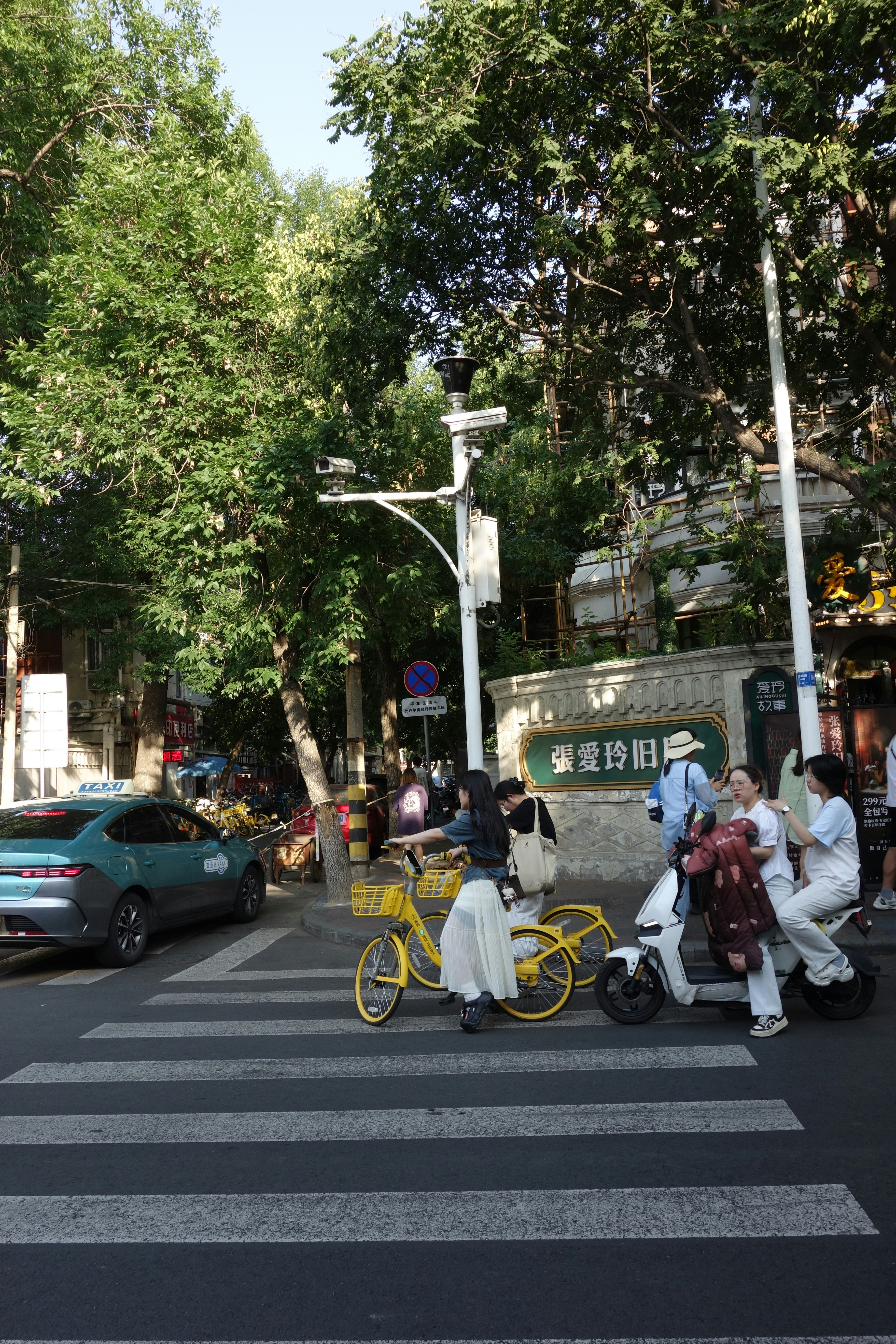 Persone in bicicletta e su uno scooter che attraversano una strada vicino a un muro di pietra