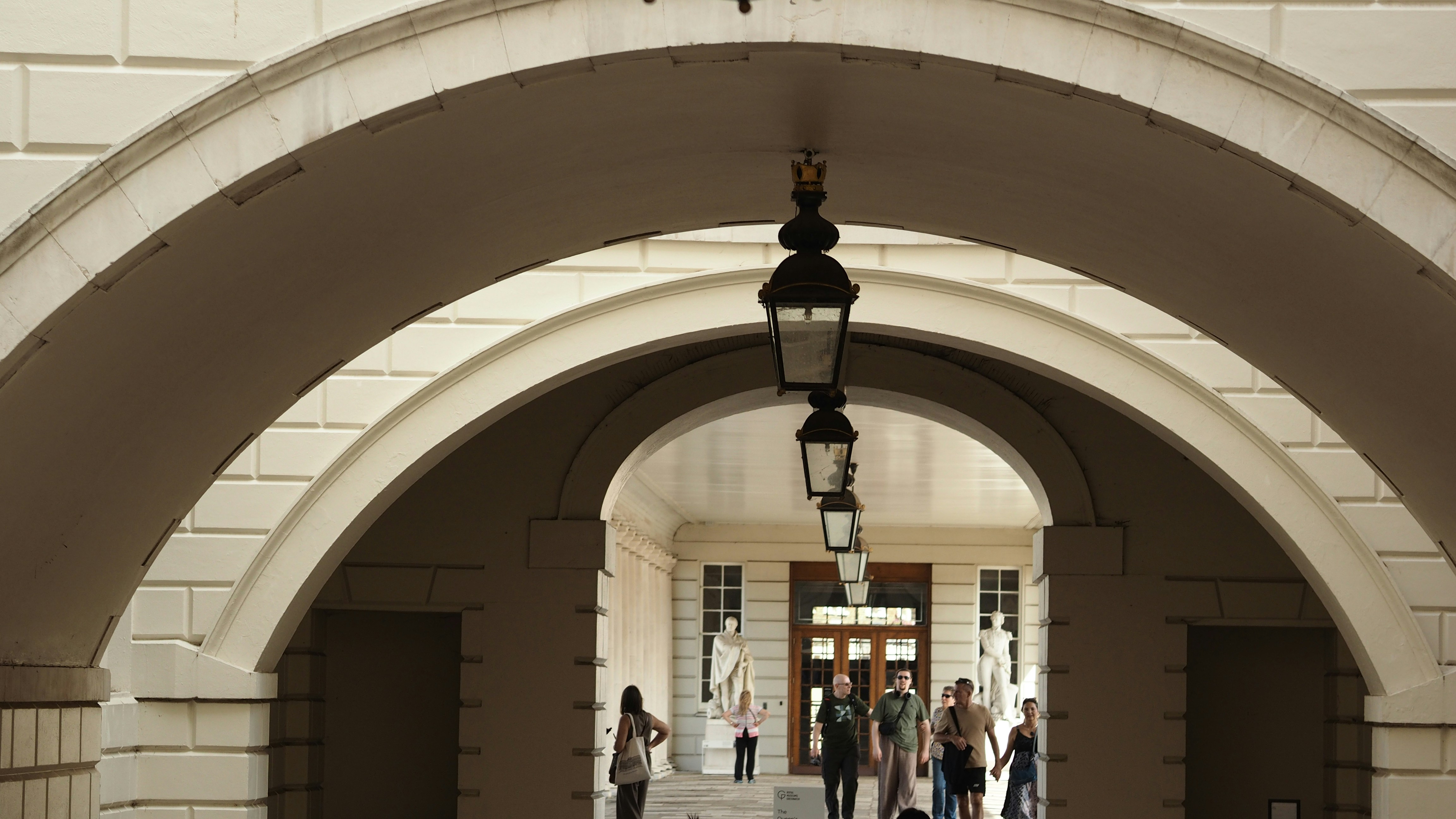 Persone che camminano attraverso una serie di archi di pietra con lanterne appese a Londra