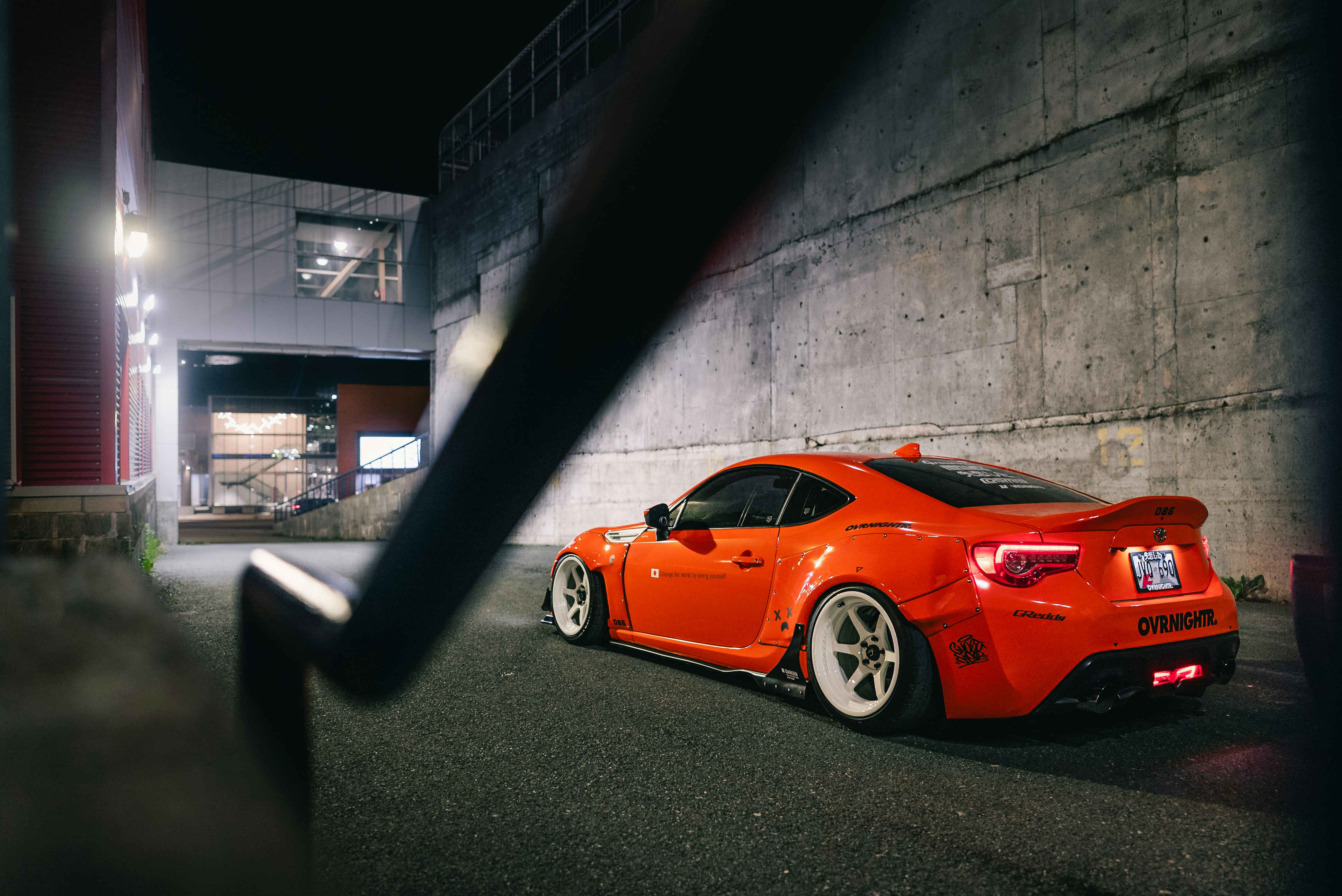 An orange modified sports car parked in a concrete alleyway at night