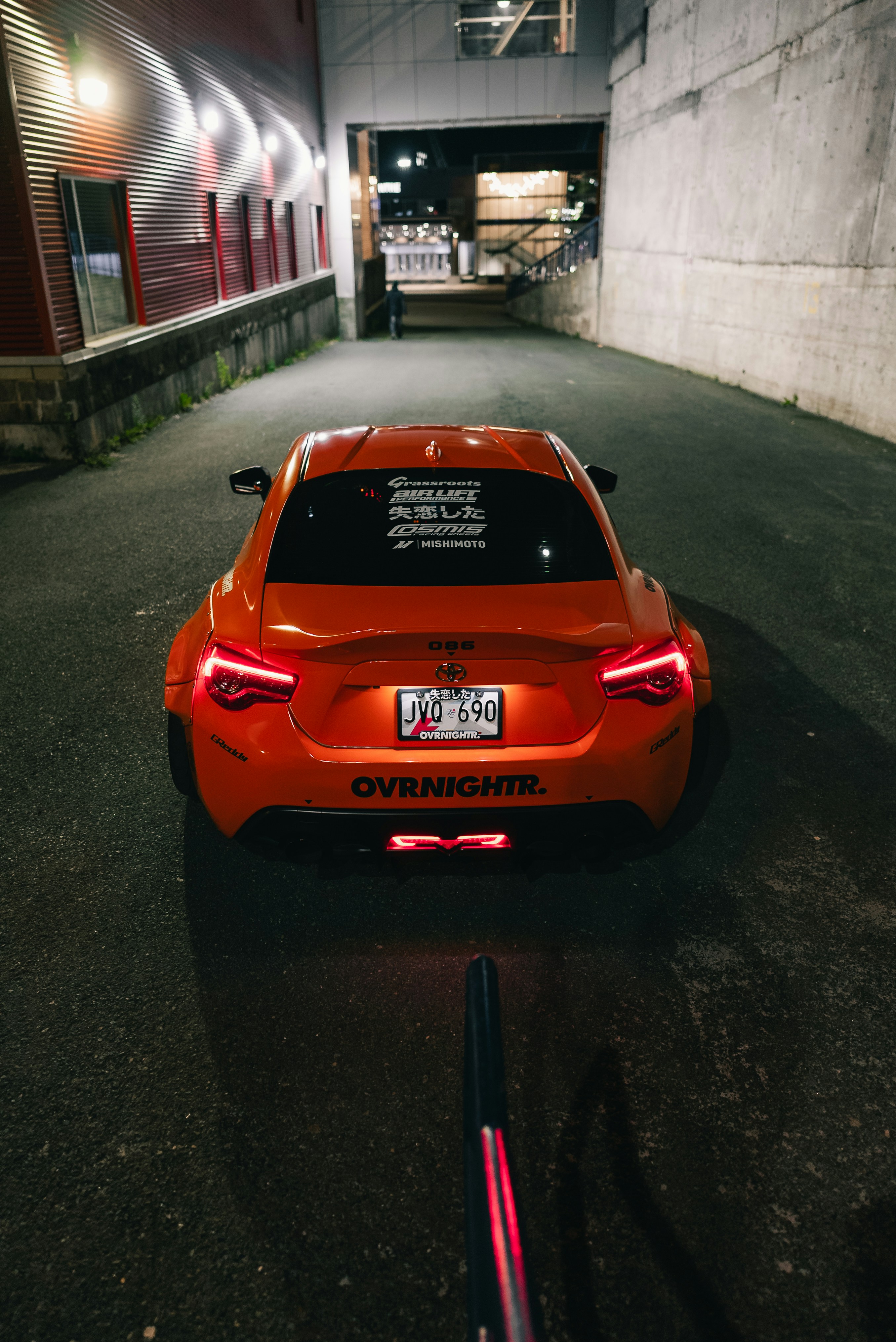 An orange sports car parked in a narrow alleyway at night