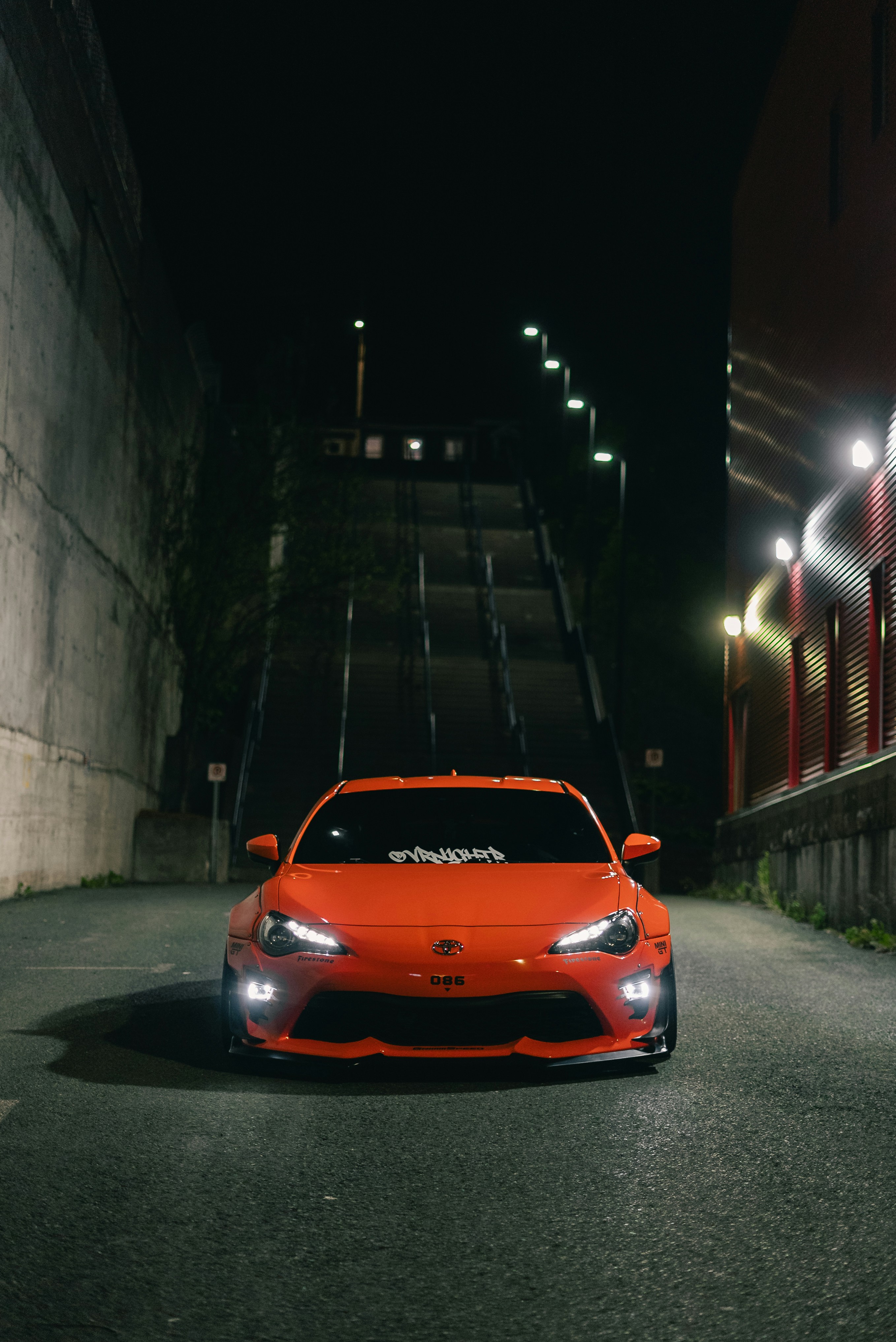 An orange sports car parked in a dark alleyway at night