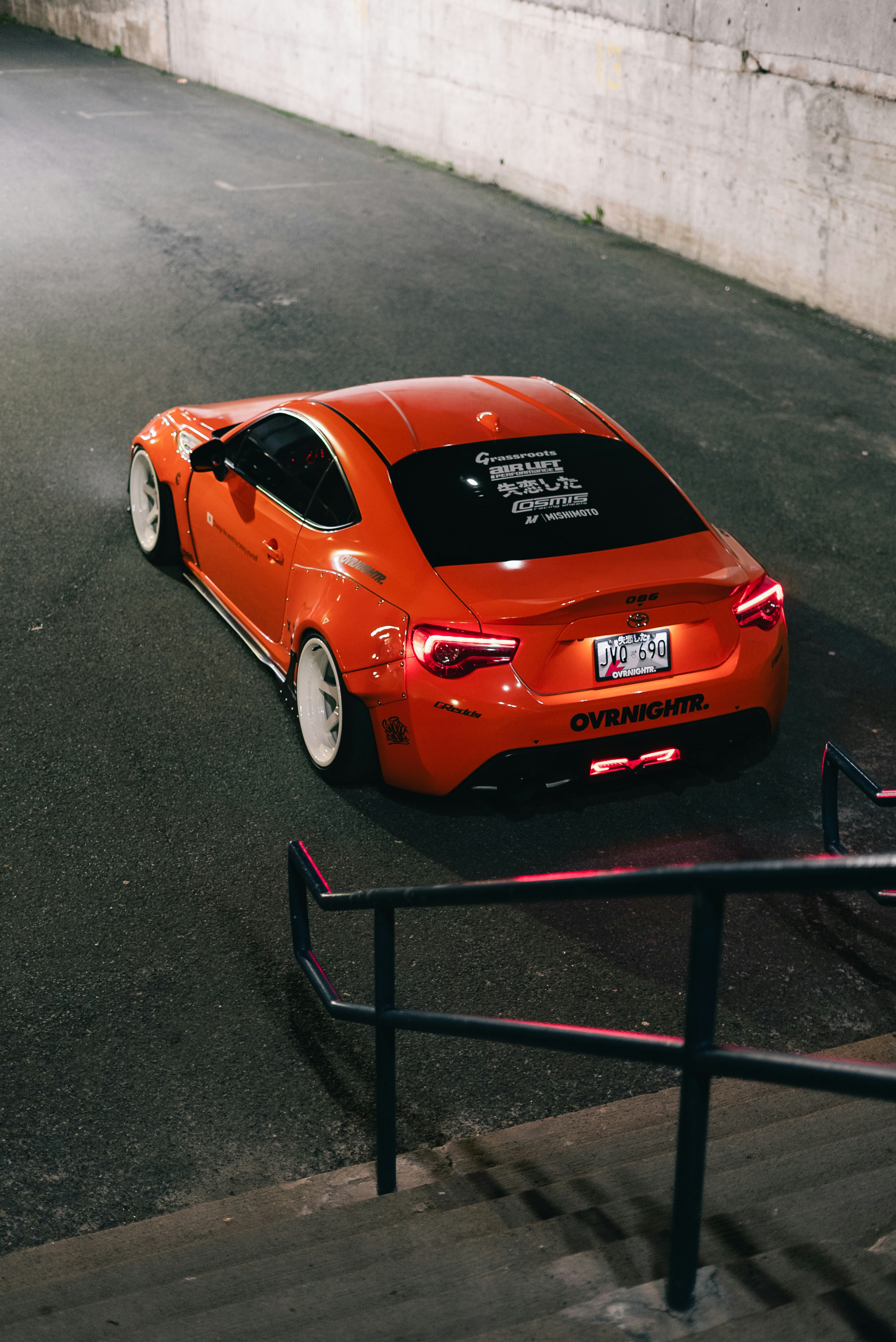 An orange Toyota 86 sports car with white wheels parked on asphalt at night