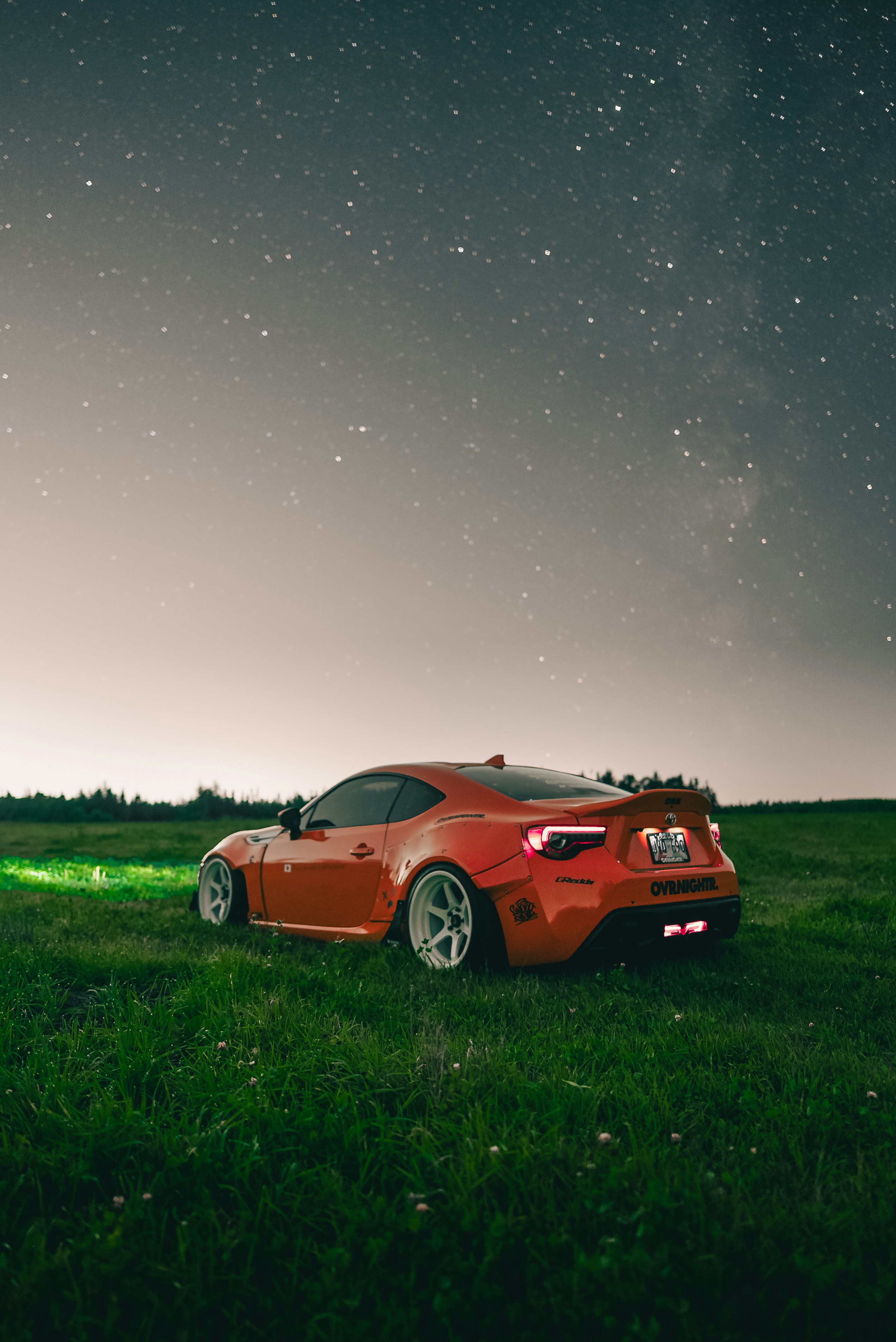 An orange sports car parked in a grassy field under a starry night sky