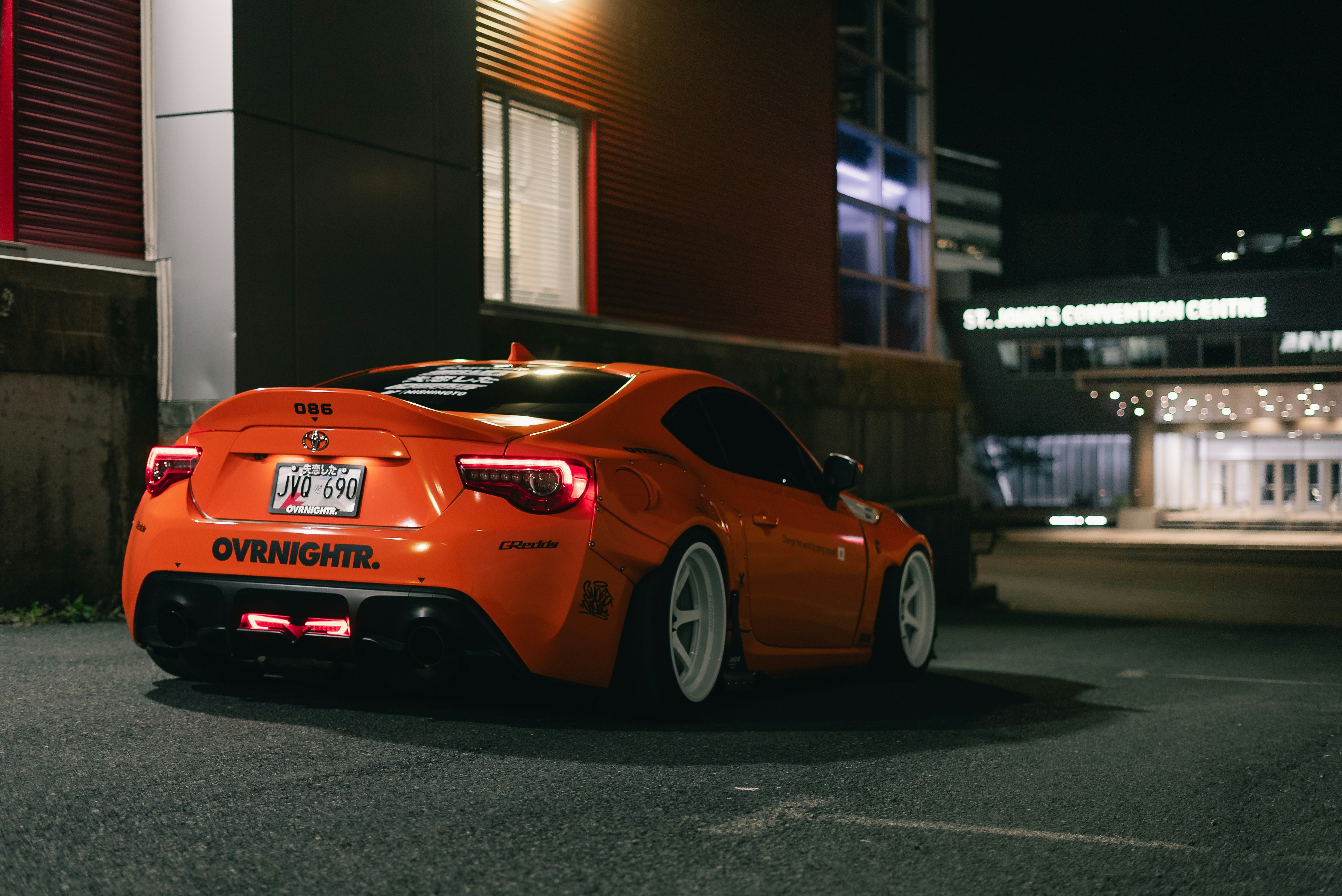 An orange modified sports car parked at night near the St. John's Convention Centre