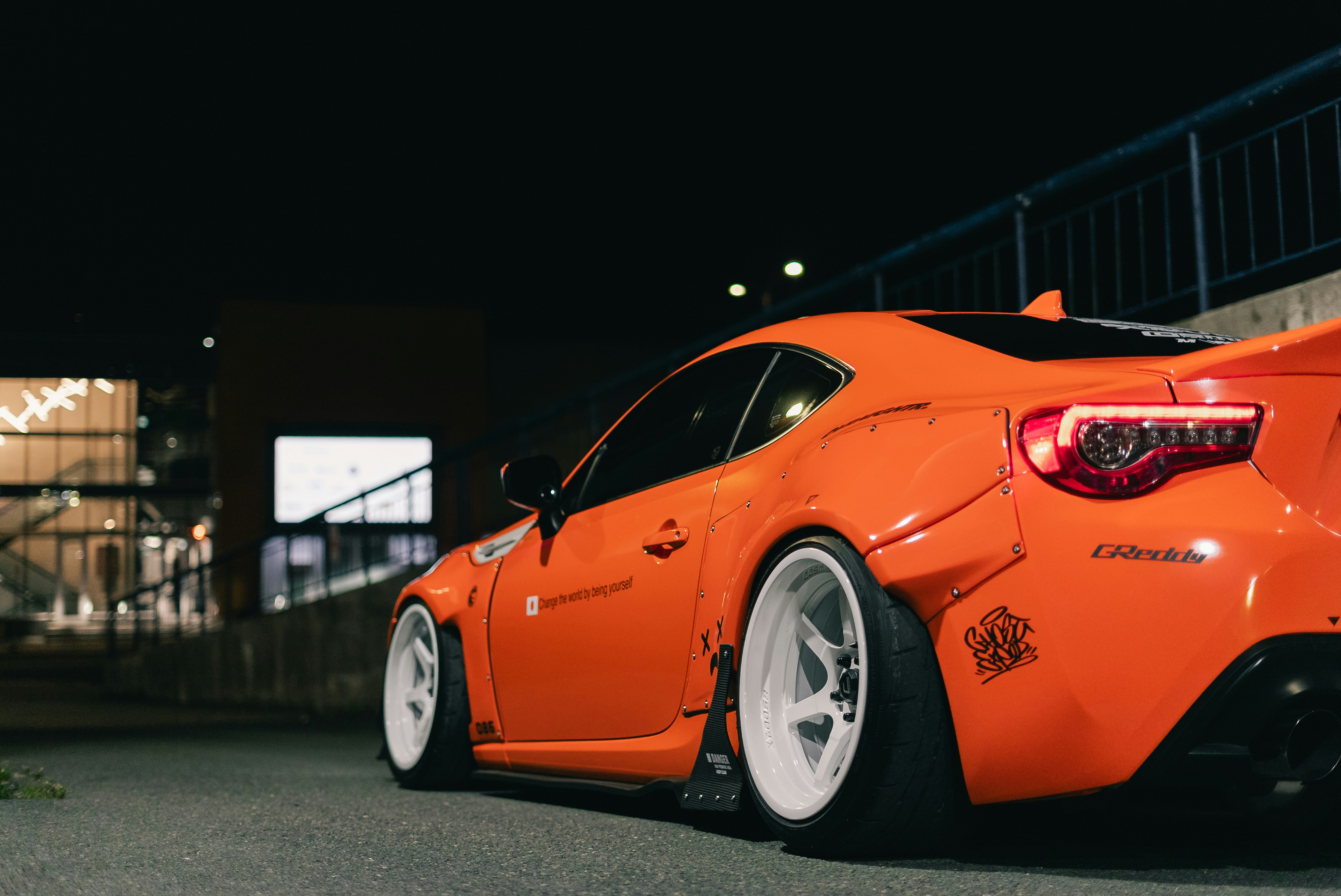 A bright orange sports car with white wheels parked on asphalt at night