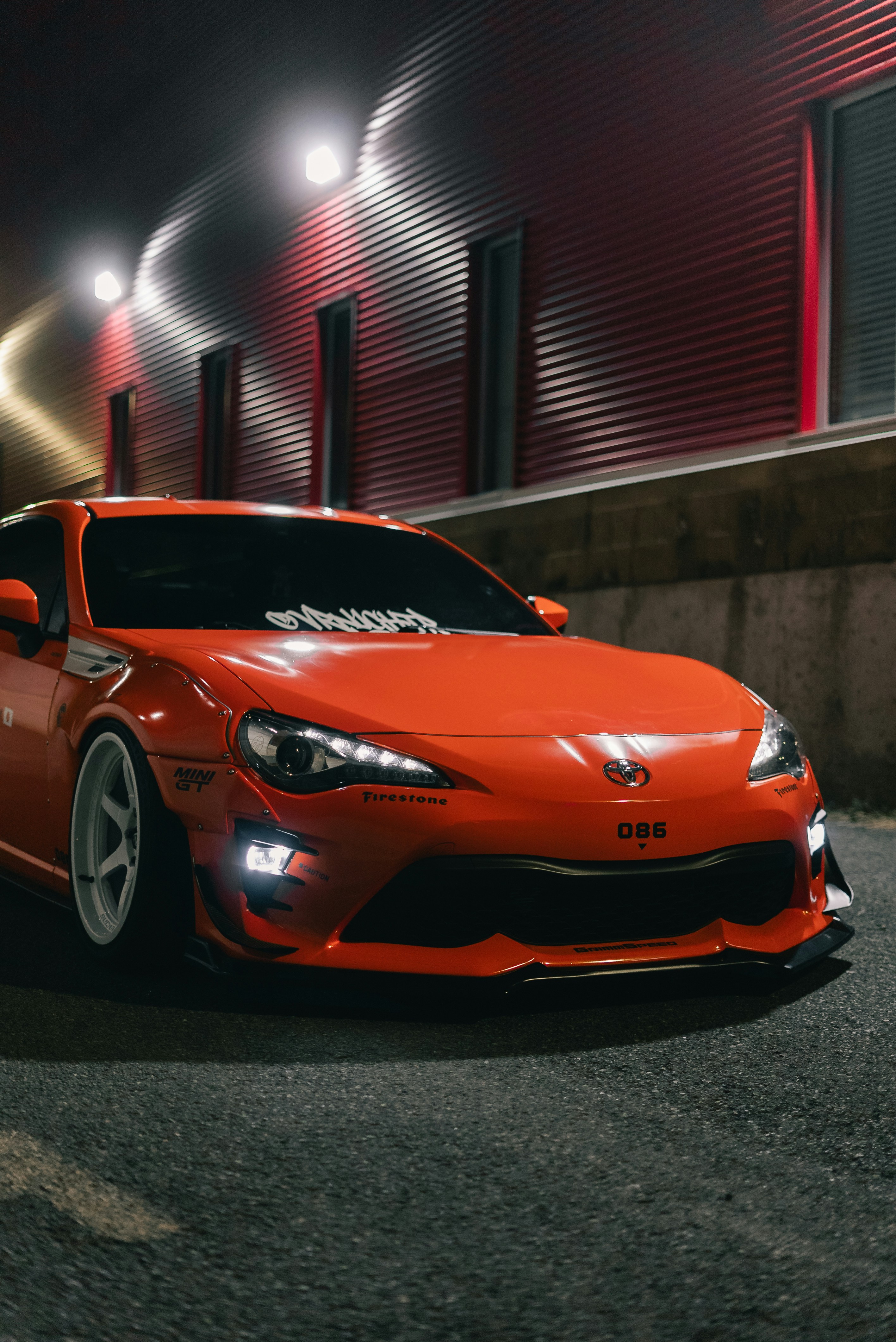 An orange sports car with white wheels parked beside a red corrugated wall