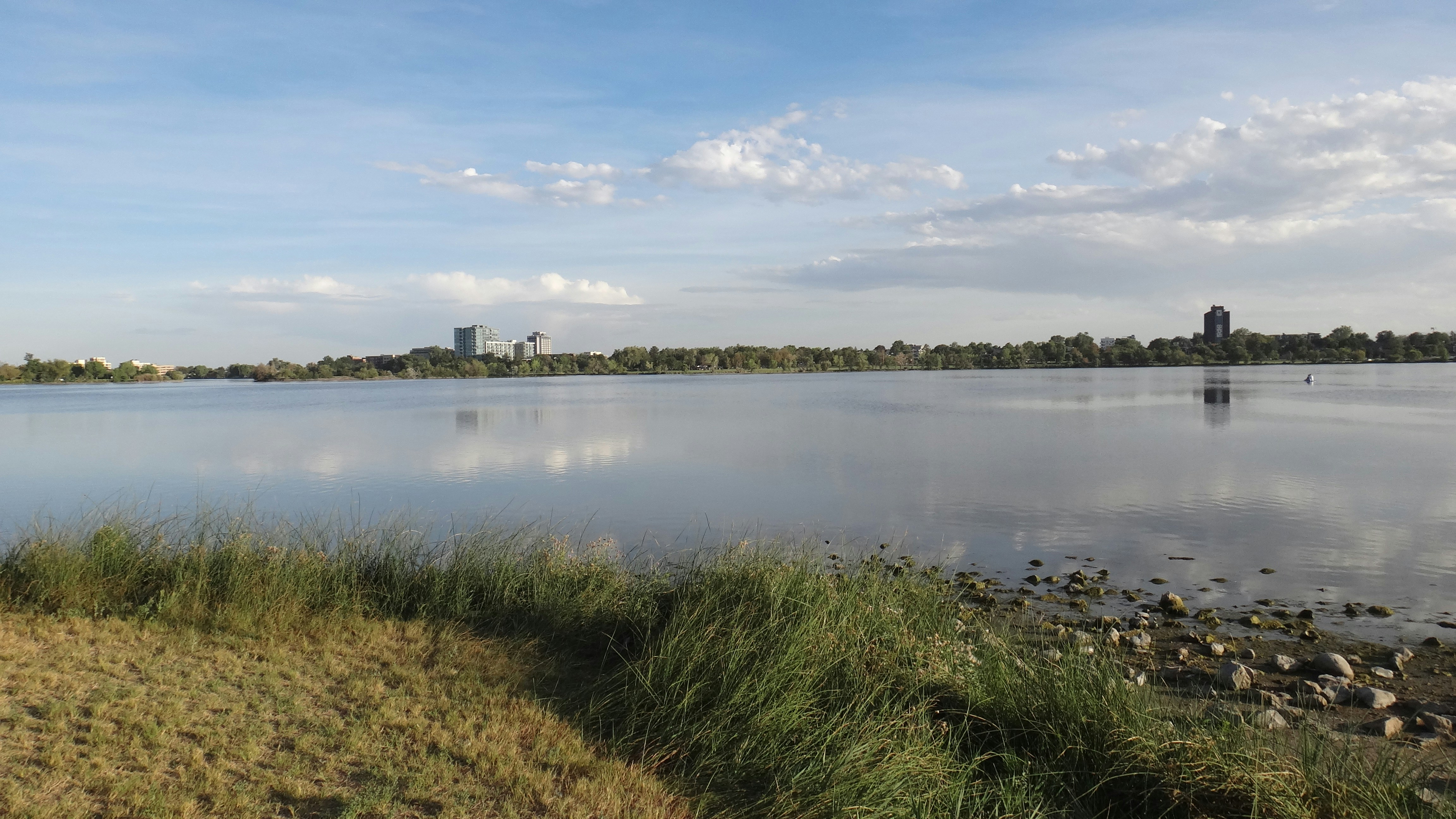 A calm lake with a distant city skyline under a blue sky