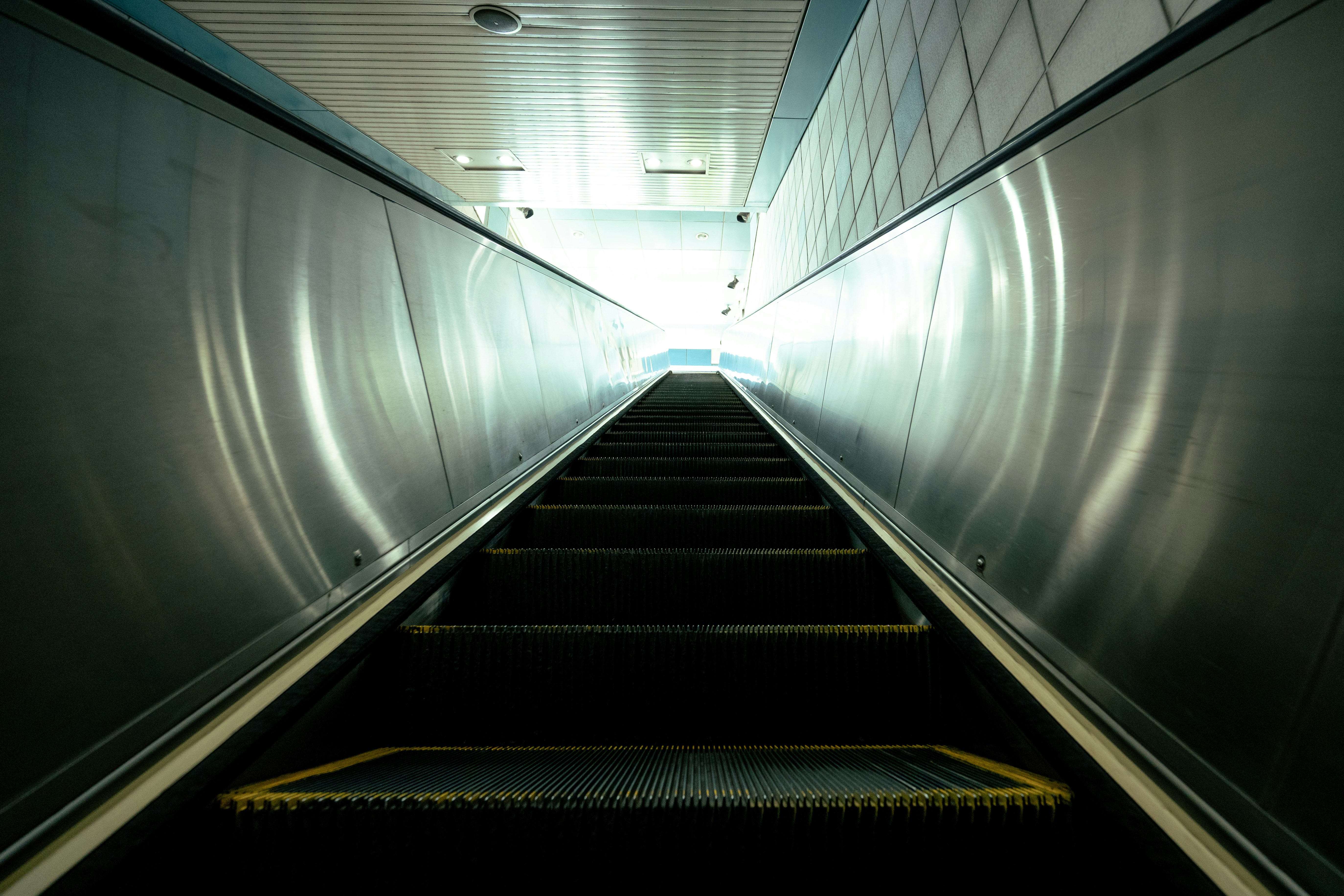 Eine leere Rolltreppe mit metallischen Seitenpaneelen, die zu einem hellen Licht führen